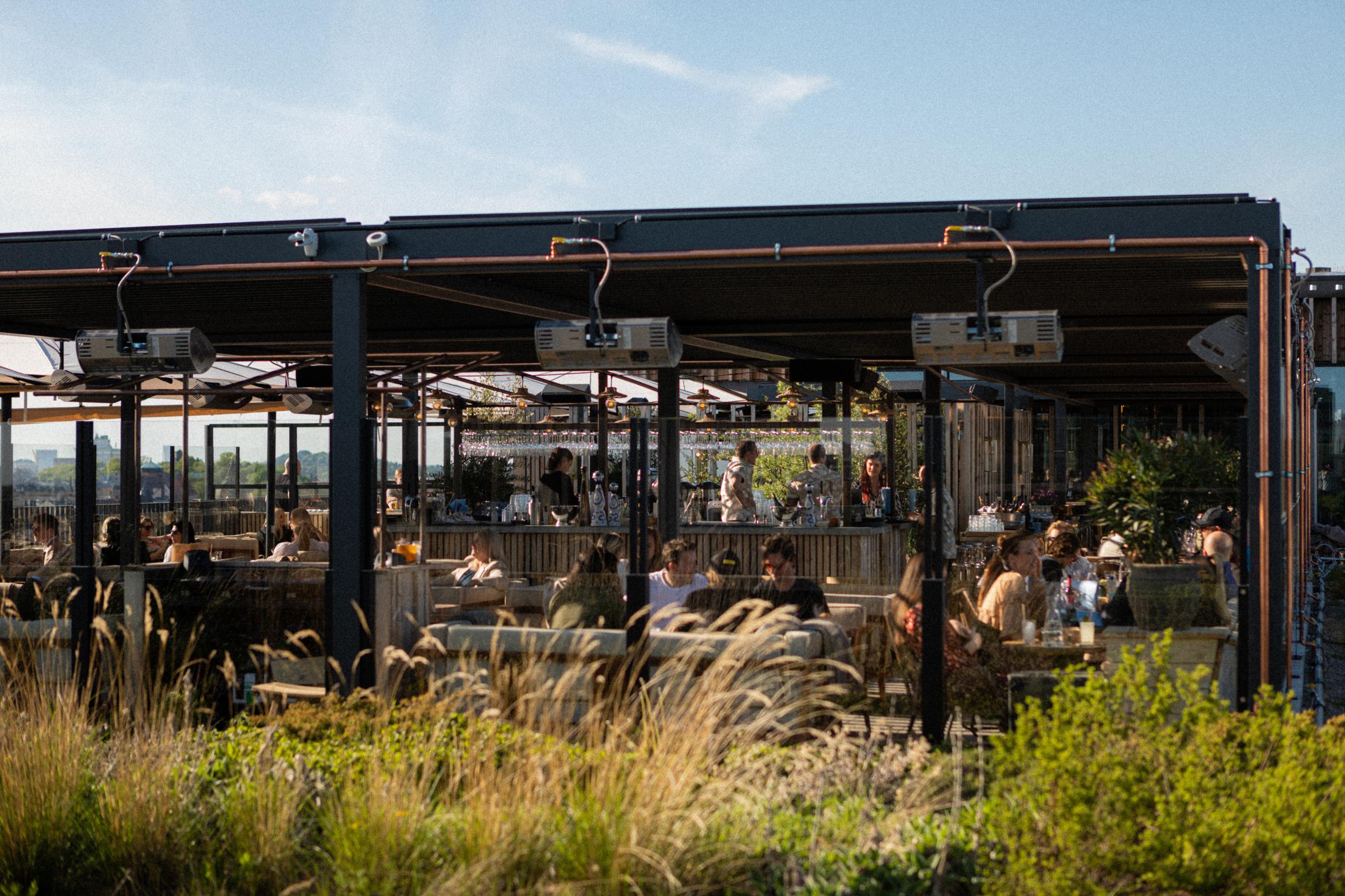 Mensen zitten op een zonnige dag bij rooftopbar Tetto.