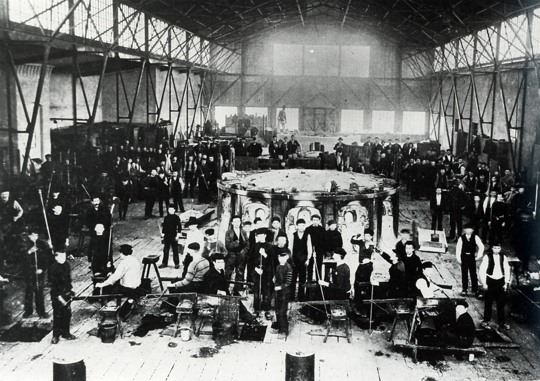 Zwart-witfoto van glasblazers aan het werk rond een grote oven in de Kosta-glasfabriek in Zweden, rond 1910. Te zien in The Glass Factory in Boda.