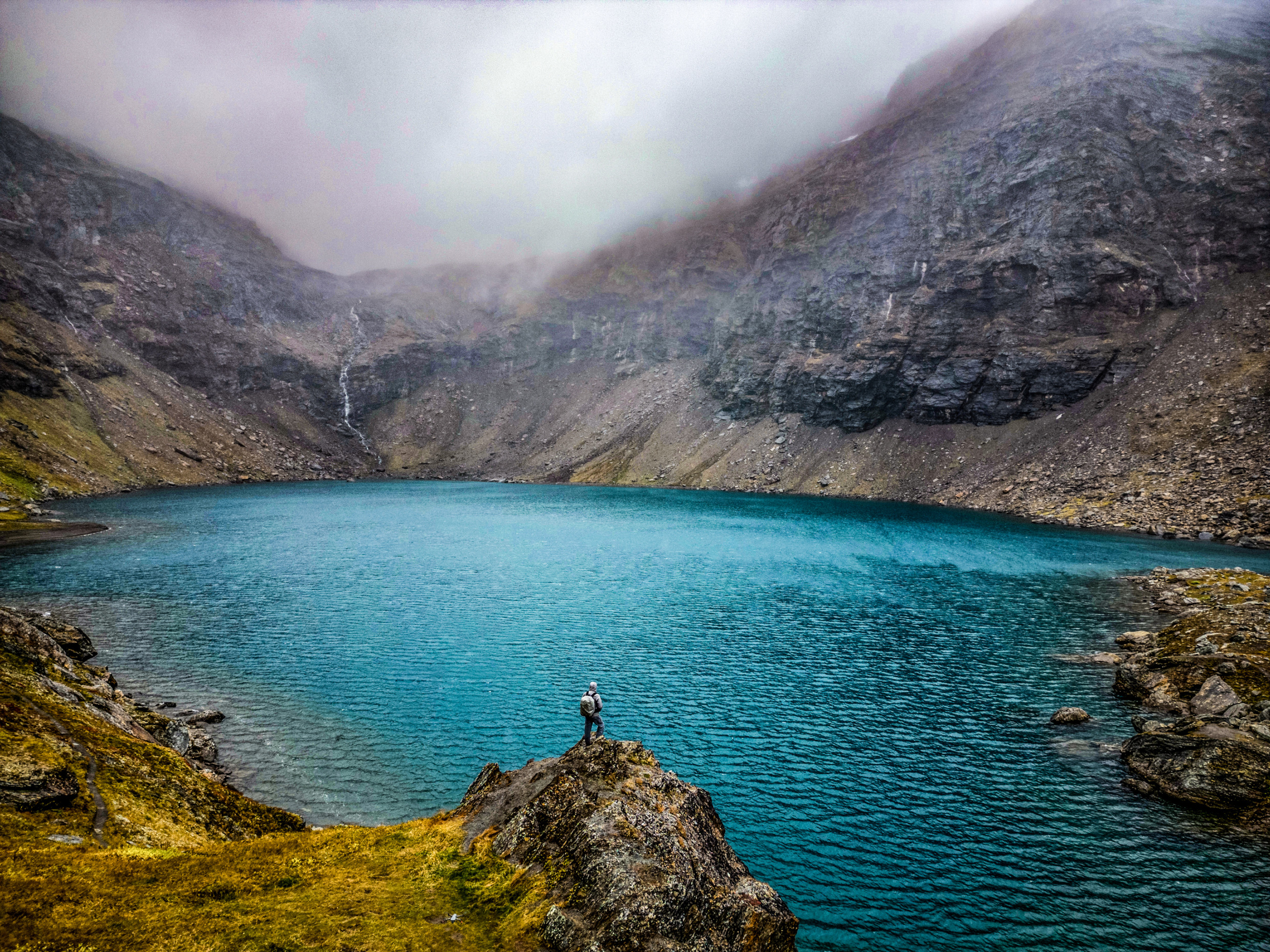 Person standing by the turquoise waters of Troll Lake (Rissajaure), surrounded by steep, rocky mountains in Swedish Lapland.