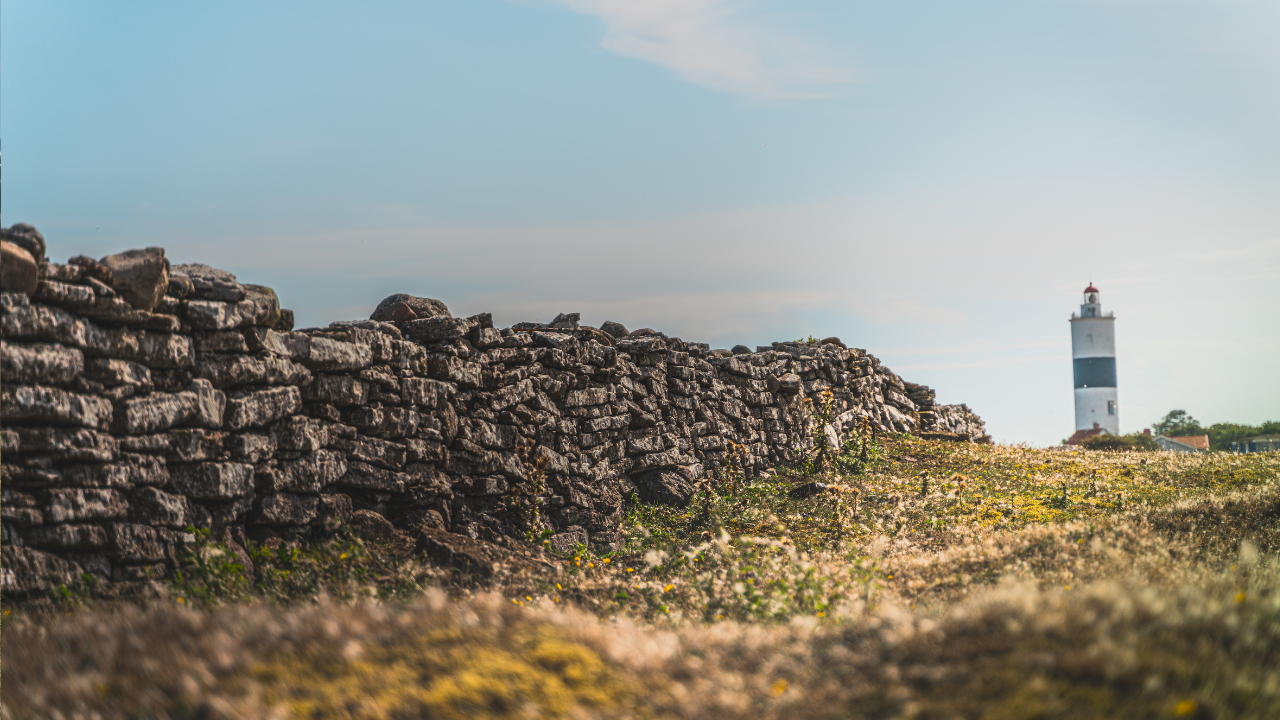 Hinter einer alten Kalksteinmauer steht ein Leuchtturm in der weiten Landschaft von Süd-Öland.