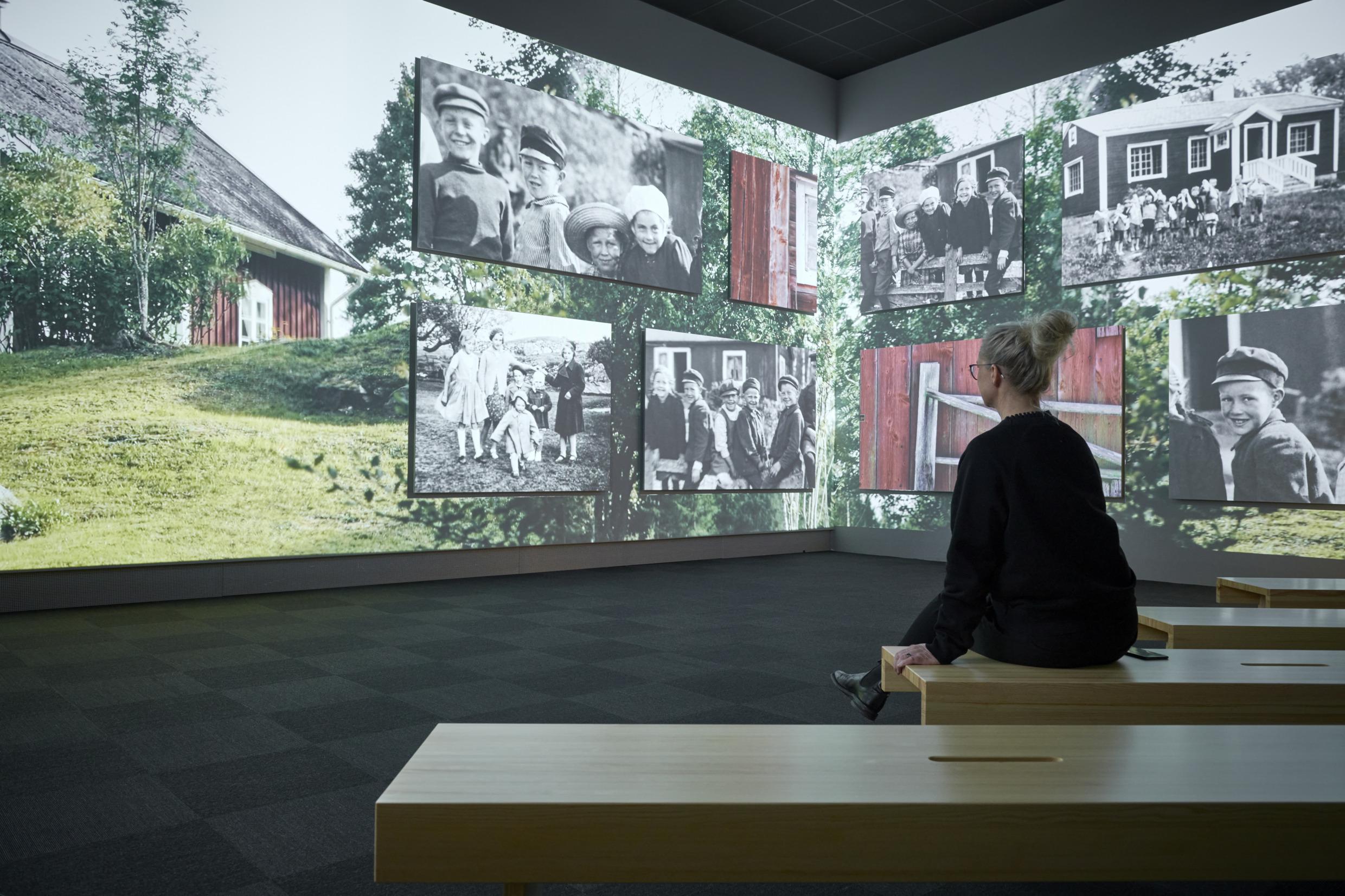 Eine Frau sitzt in einem Raum und betrachtet Bilder von Småland.