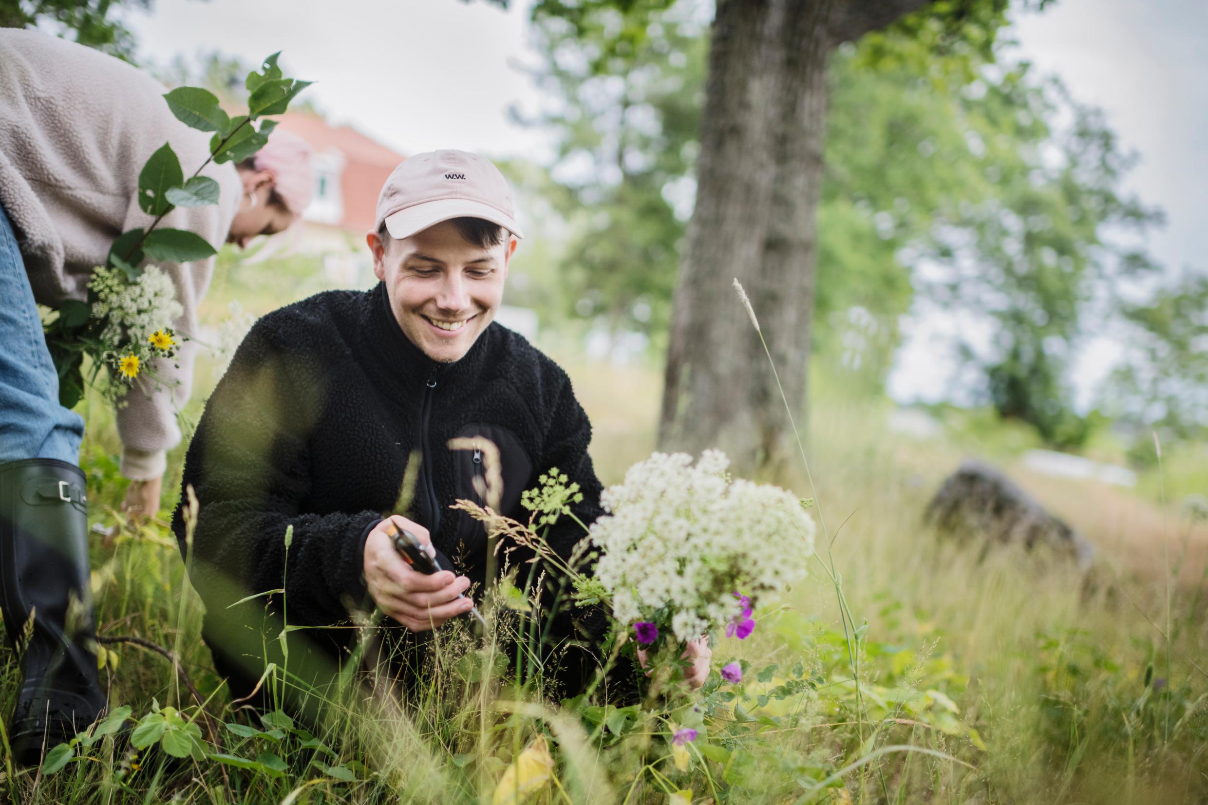 Een man zit op zijn hurken in een bloemrijk veld.