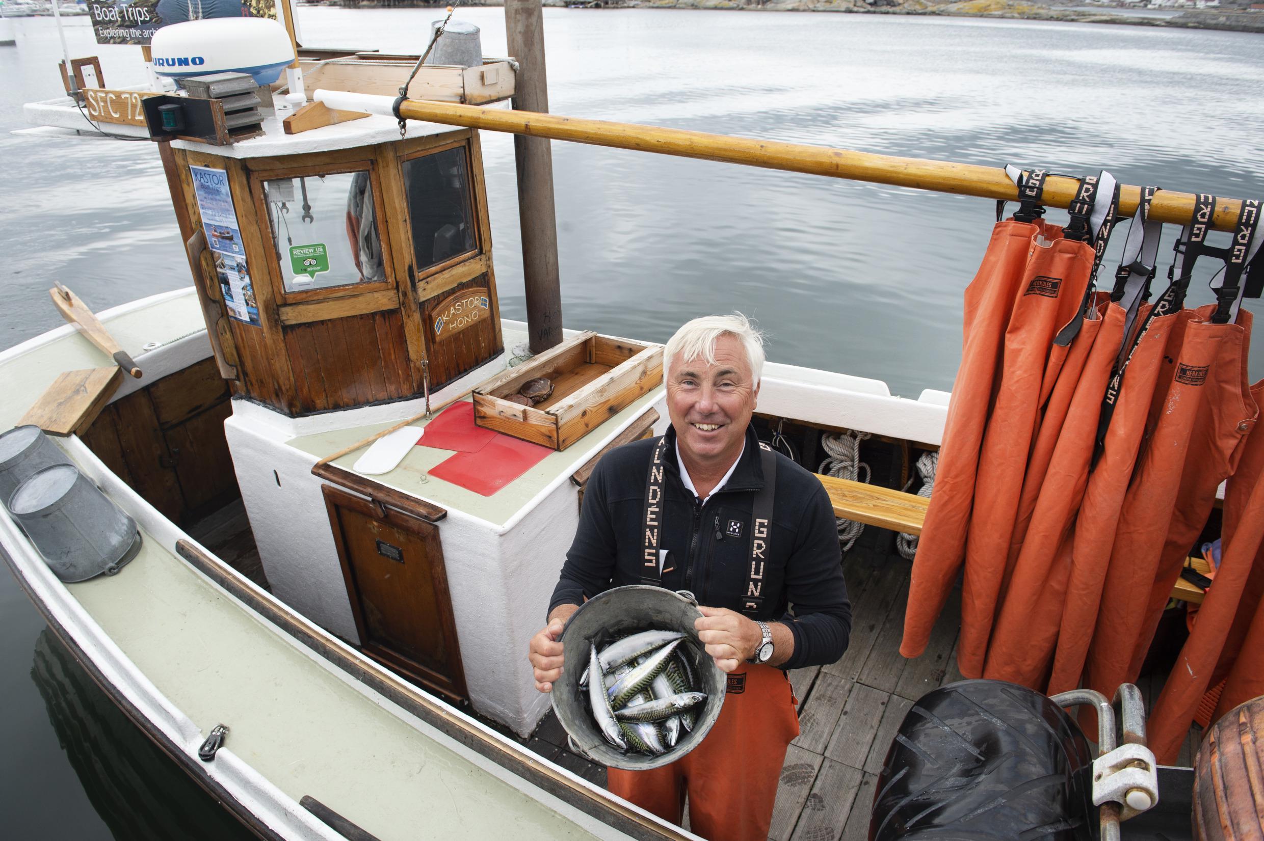A man standing in a fishing boat holding a bucket filled with fish.