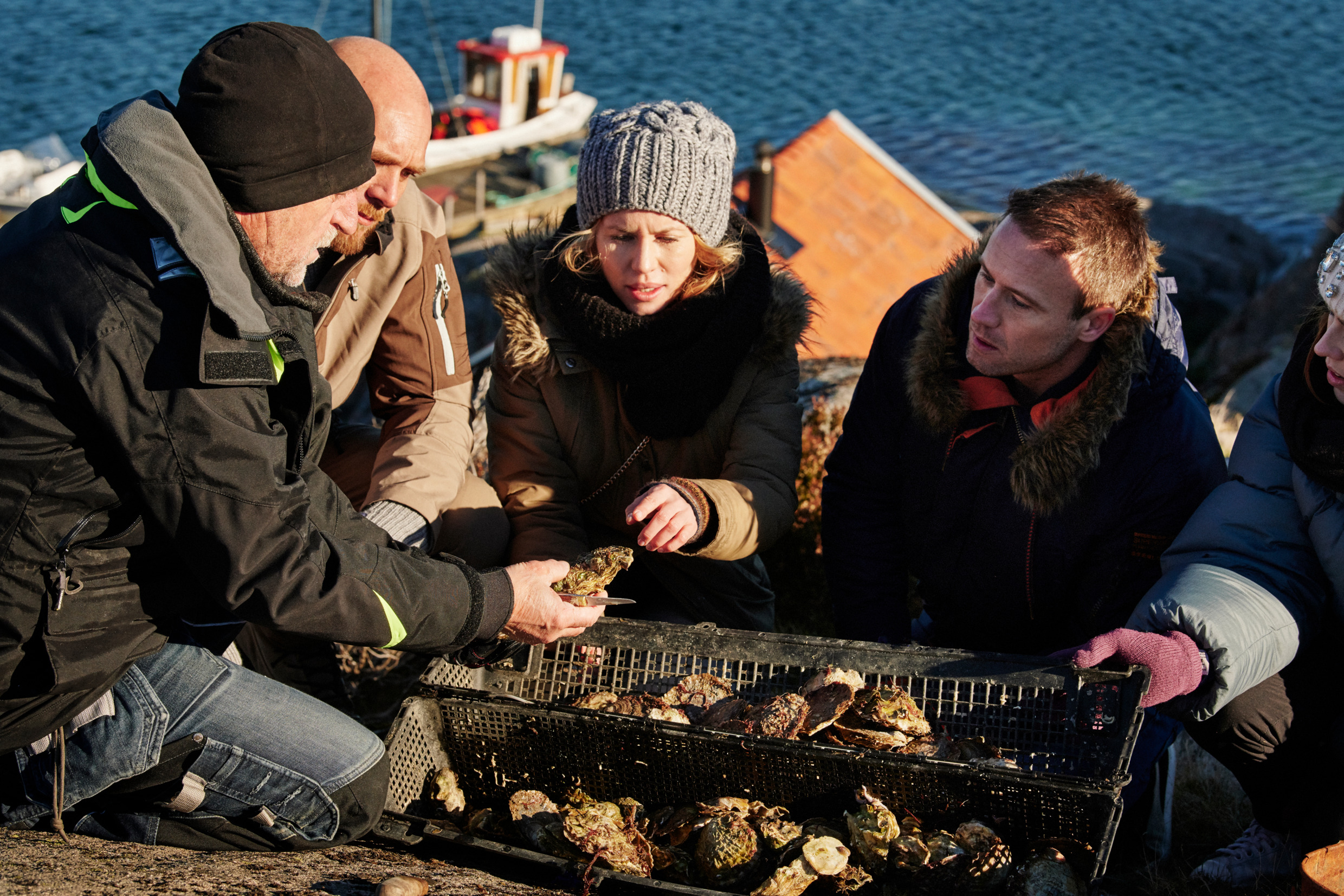 Tree men and a woman on the cliff by the sea tasting oysters.