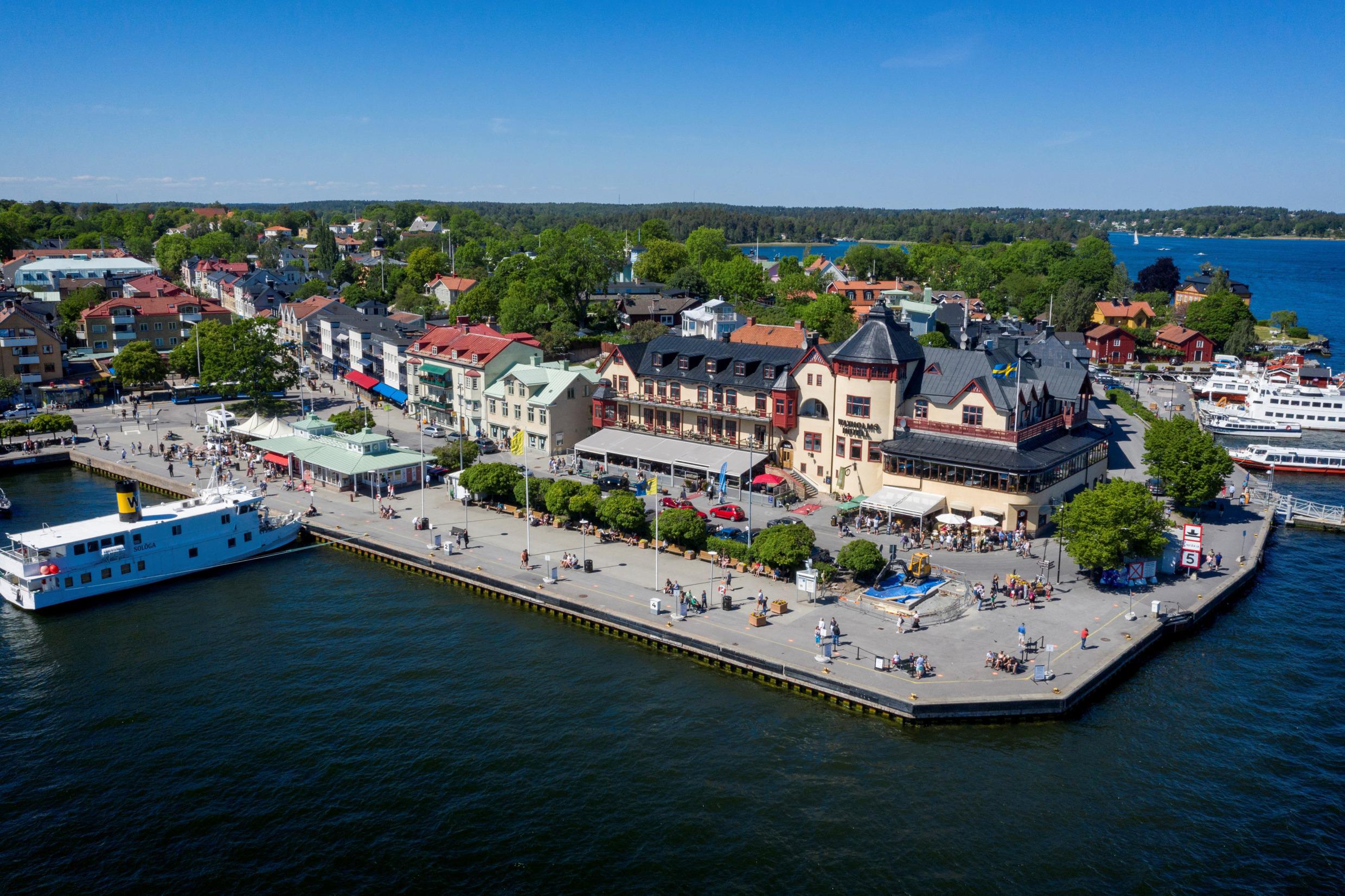 Aerial view of Waxholms hotel and the small town Vaxholm in the archipelago. There are ferry boats in the harbour and people moving around.