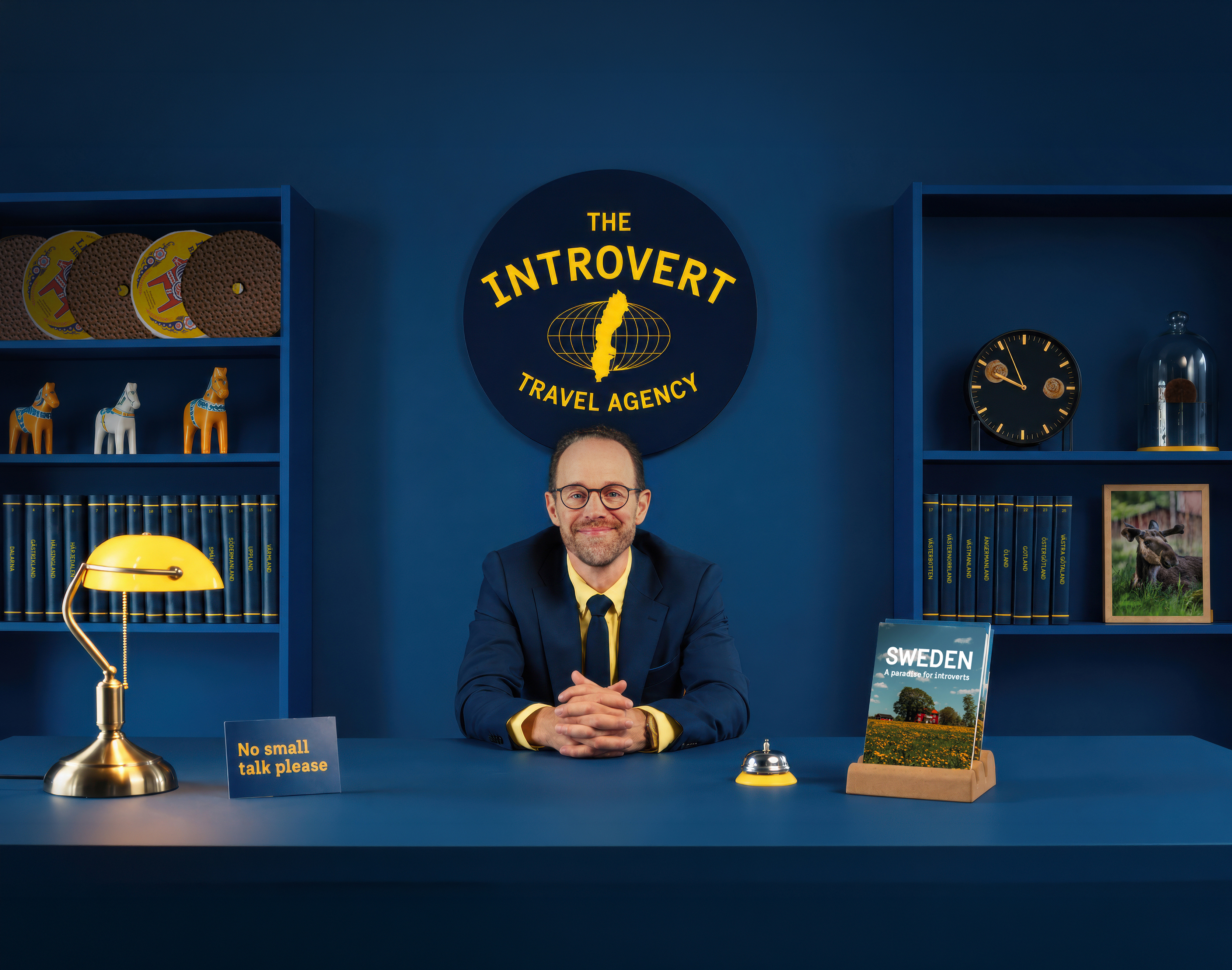 A well-dressed man sits behind the desk at The Introvert Travel Agency, ready to help travellers find their ideal Swedish getaway.