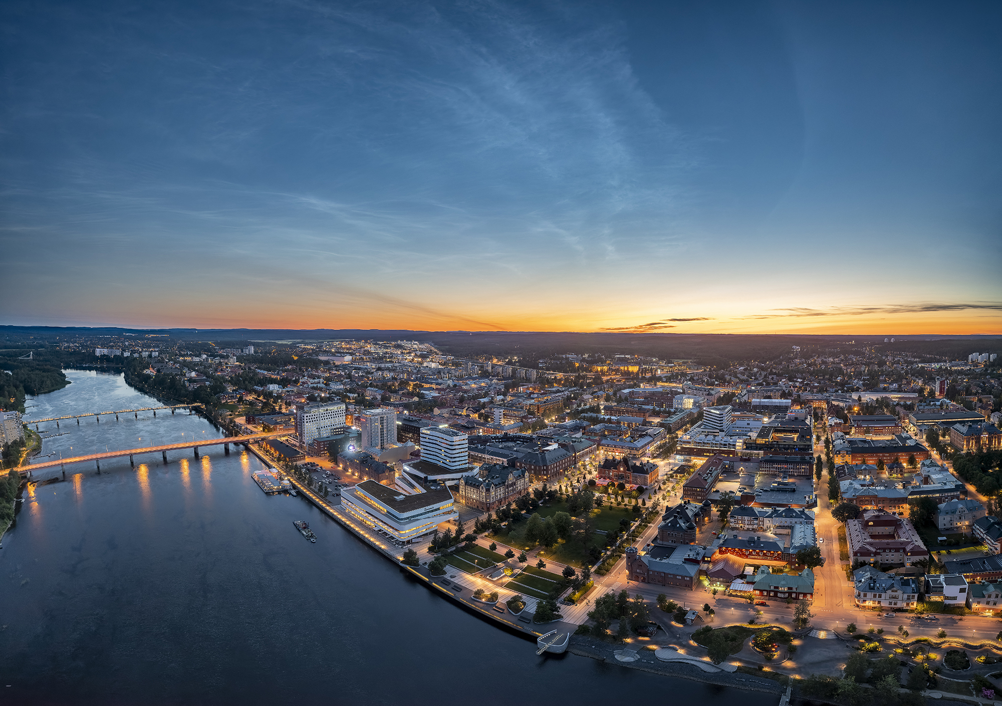 Aerial view of central Umeå at dusk, with the Ume River, bridges, illuminated streets and buildings stretching towards the horizon.