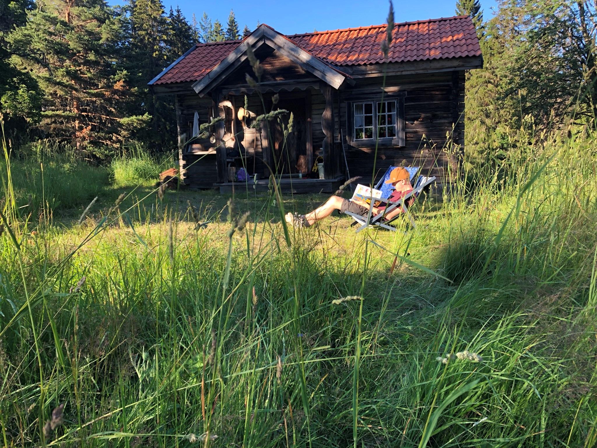 Een man zit in een ligstoel voor een klein huisje dat helemaal omringd is door groen.
