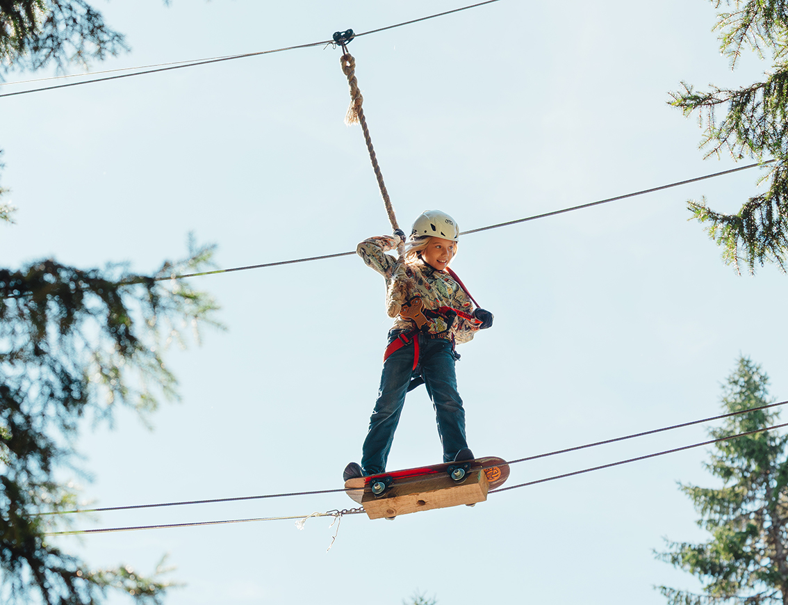 A child wearing a helmet and safety harness balances on a high ropes course at Zip Adventure Park near Umeå.