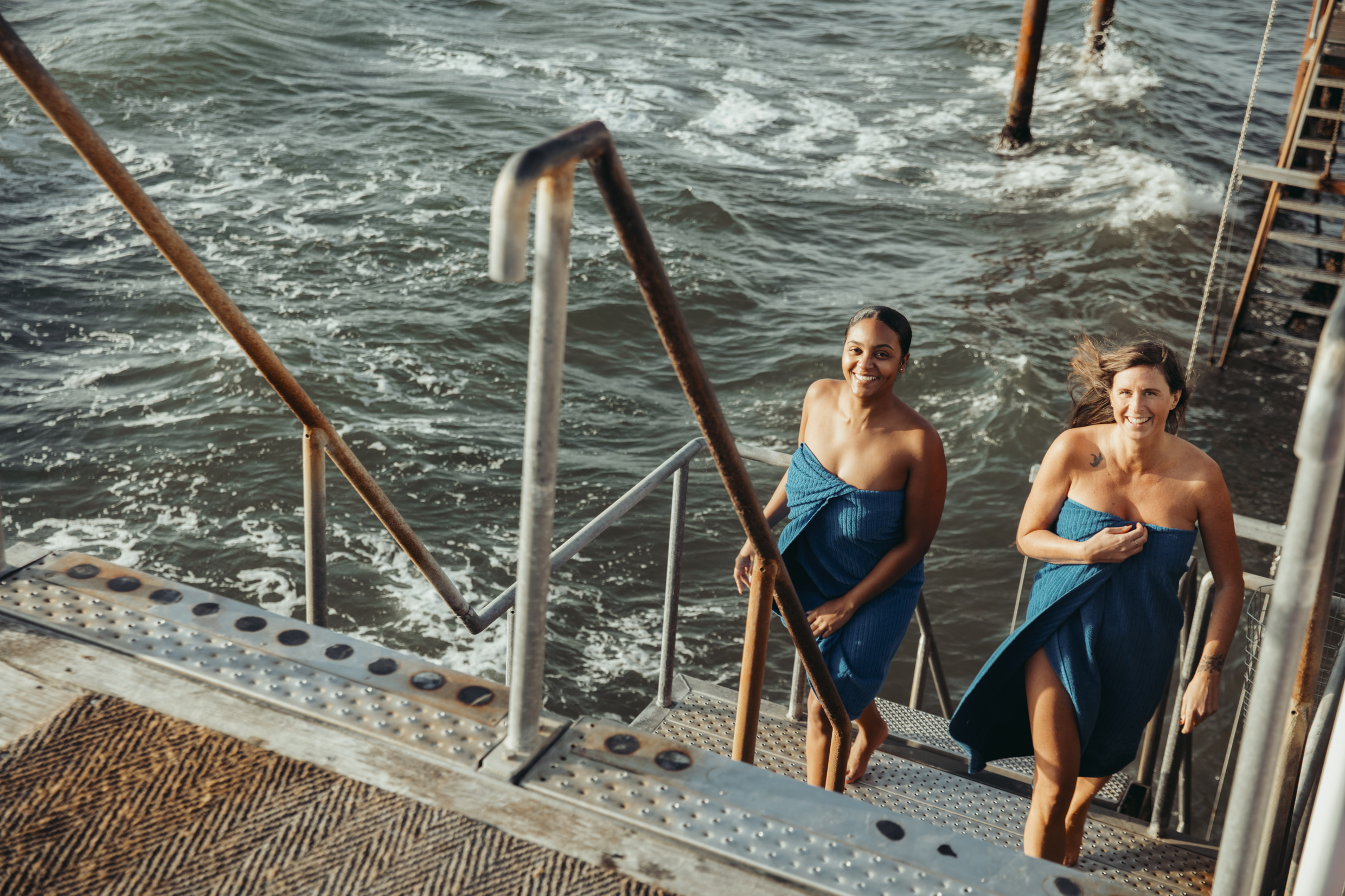 Two women smile as they emerge from a cold bath in the sea.