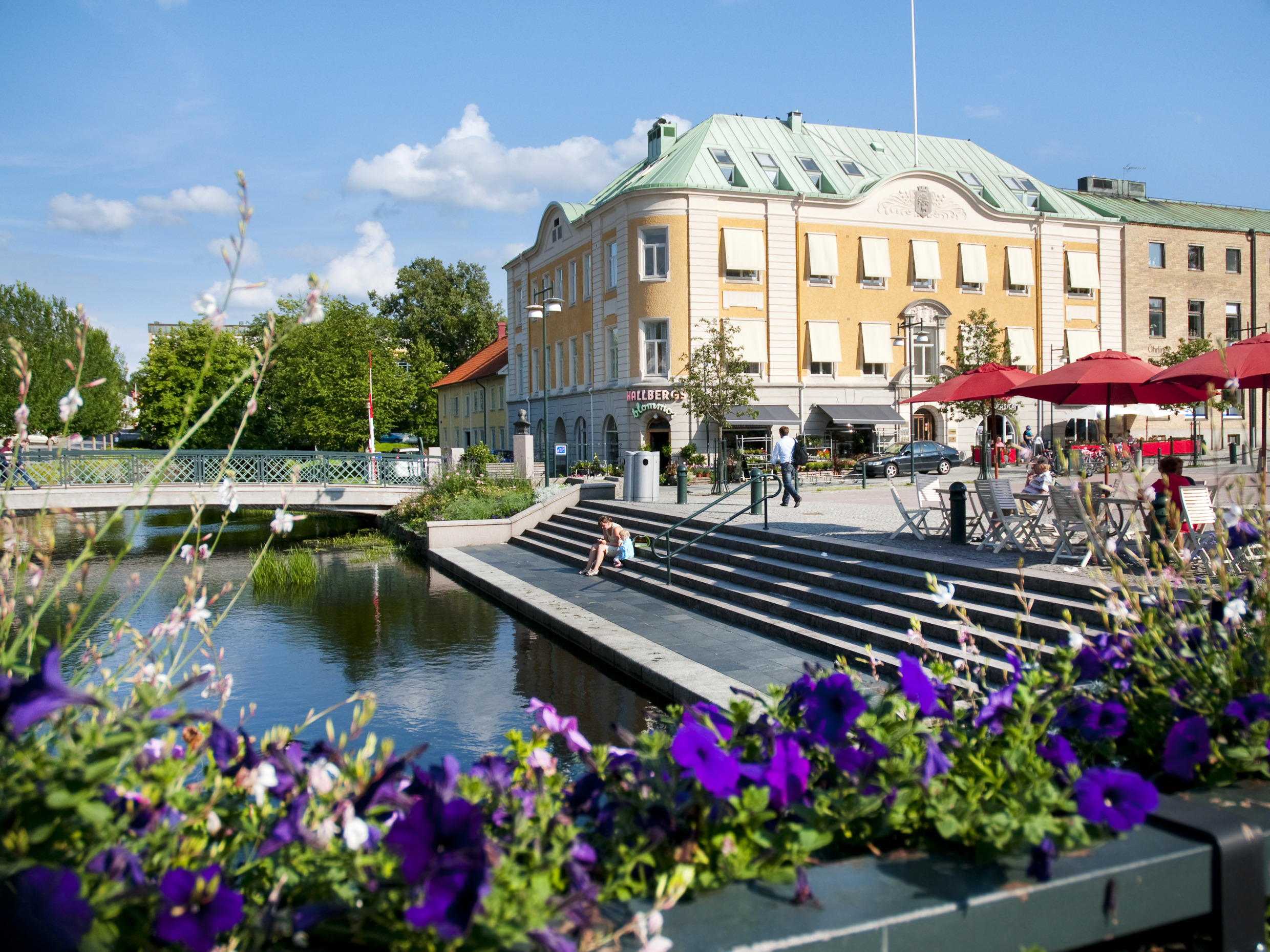 Zonnige dag in Alingsås. Stadscentrum met trappen en een brug over Lillån. Paarse bloemen op de voorgrond.