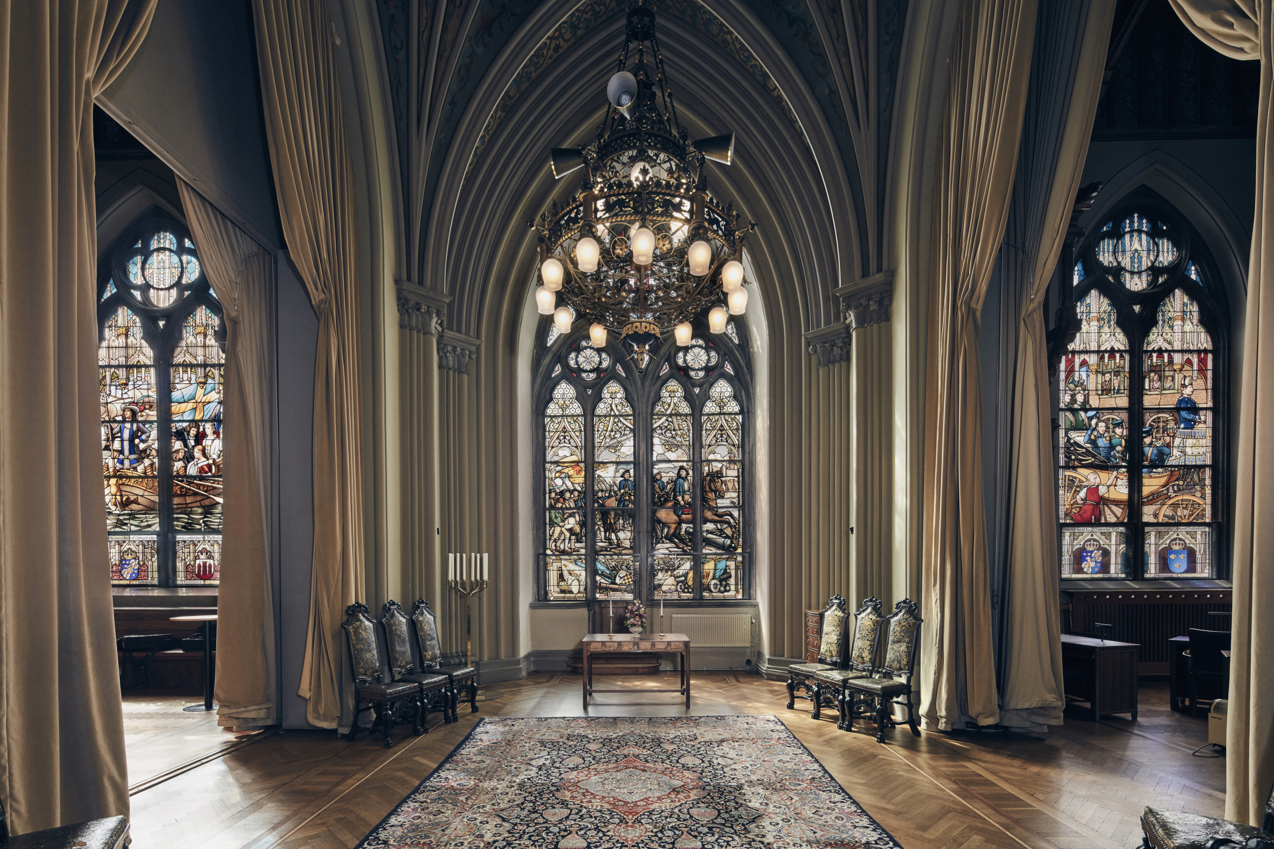 Der Hochzeitssaal im Rathaus von Helsingborg. Die Sonne scheint durch die bleiverglasten Fenster und spiegelt sich im Parkettboden des großen Raums. Ein großer Kronleuchter hängt von der hohen Decke.
