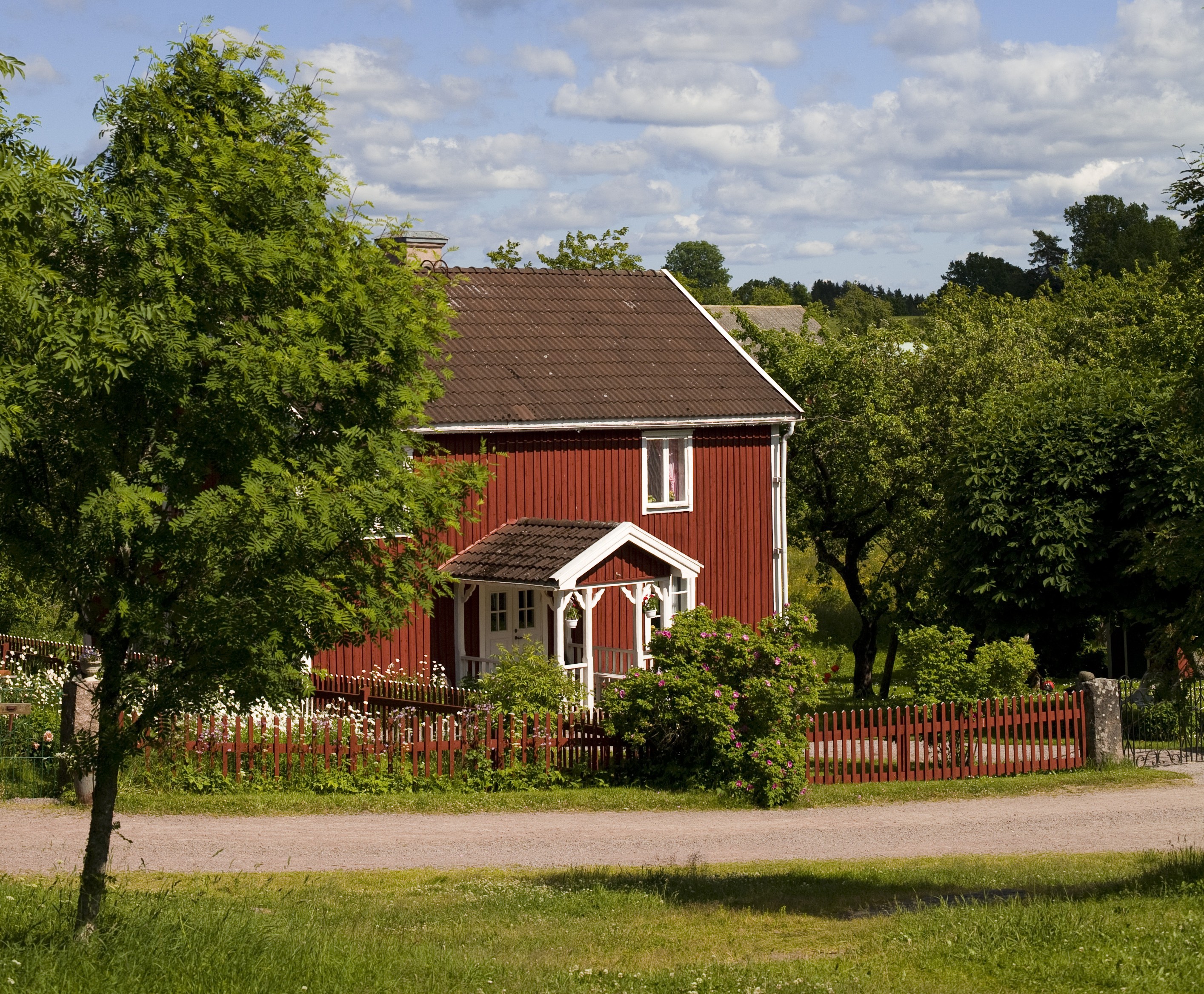 Traditionelles rotes Holzhaus, umgeben von Wiesen und Bäumen in der schwedischen Landschaft.