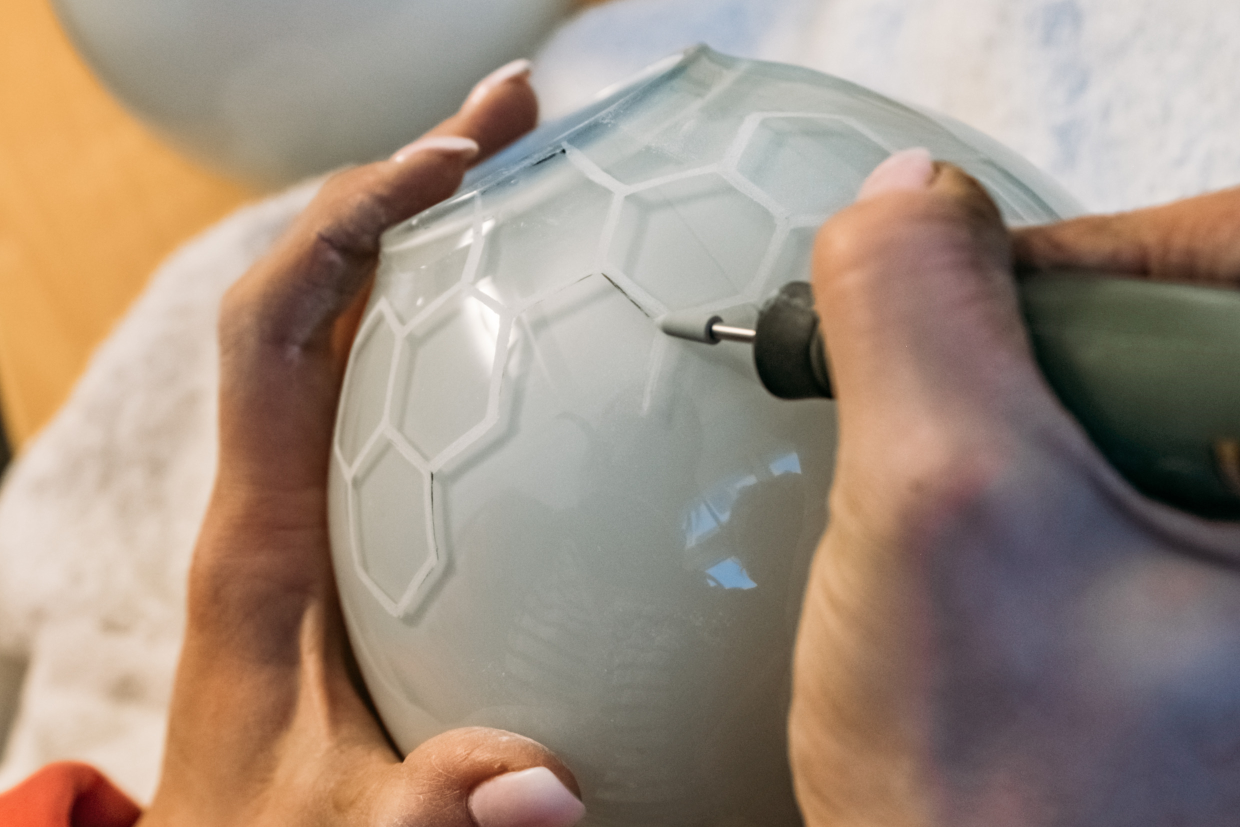 Nahaufnahme von Händen, die bei Åre Glashytta in Duved ein geometrisches Muster in ein mattiertes Glasobjekt gravieren.