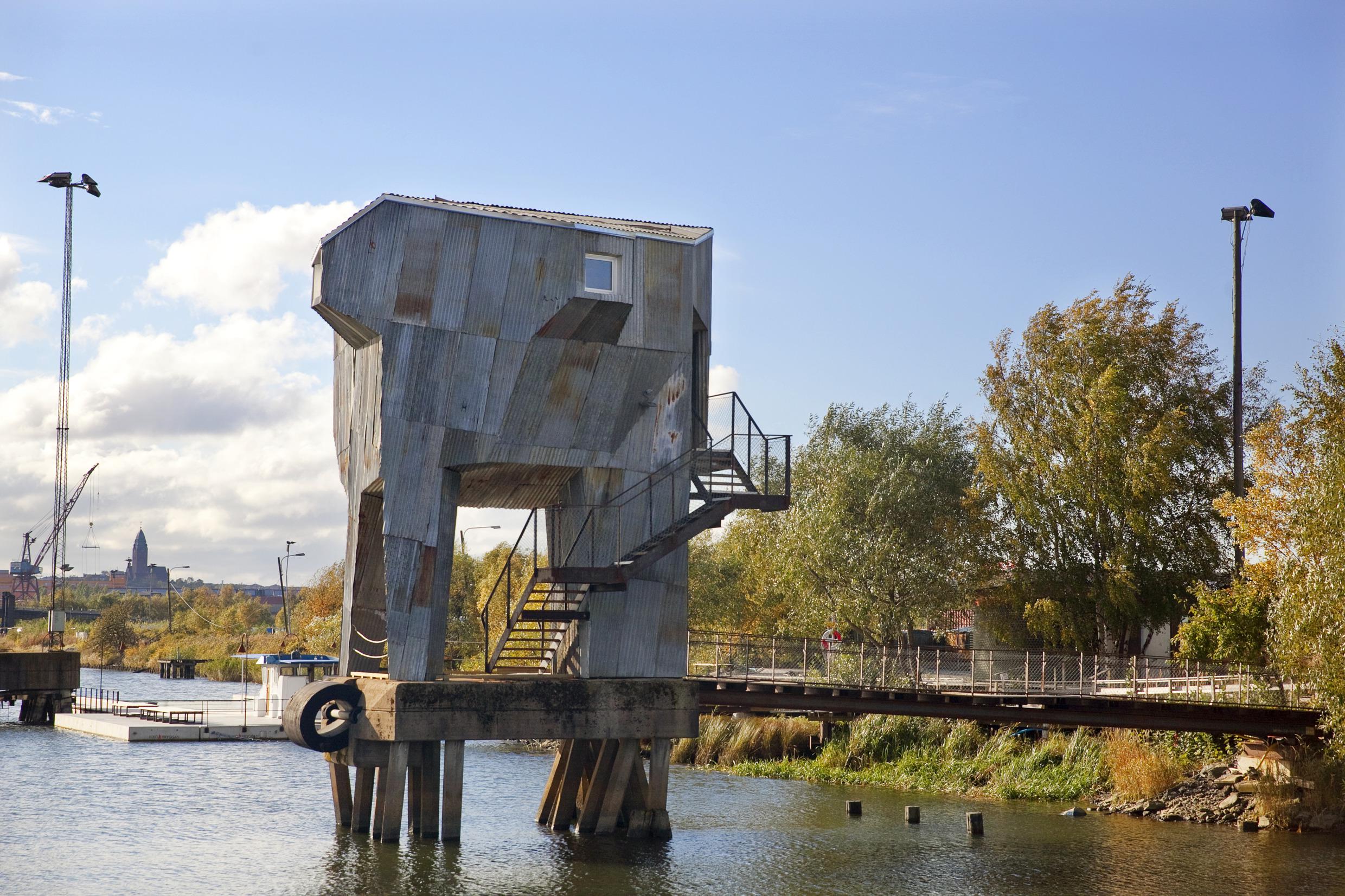 Tall sauna in gray made of recycables, standing on a platform above the water in Frihamnen, Gothenburg.