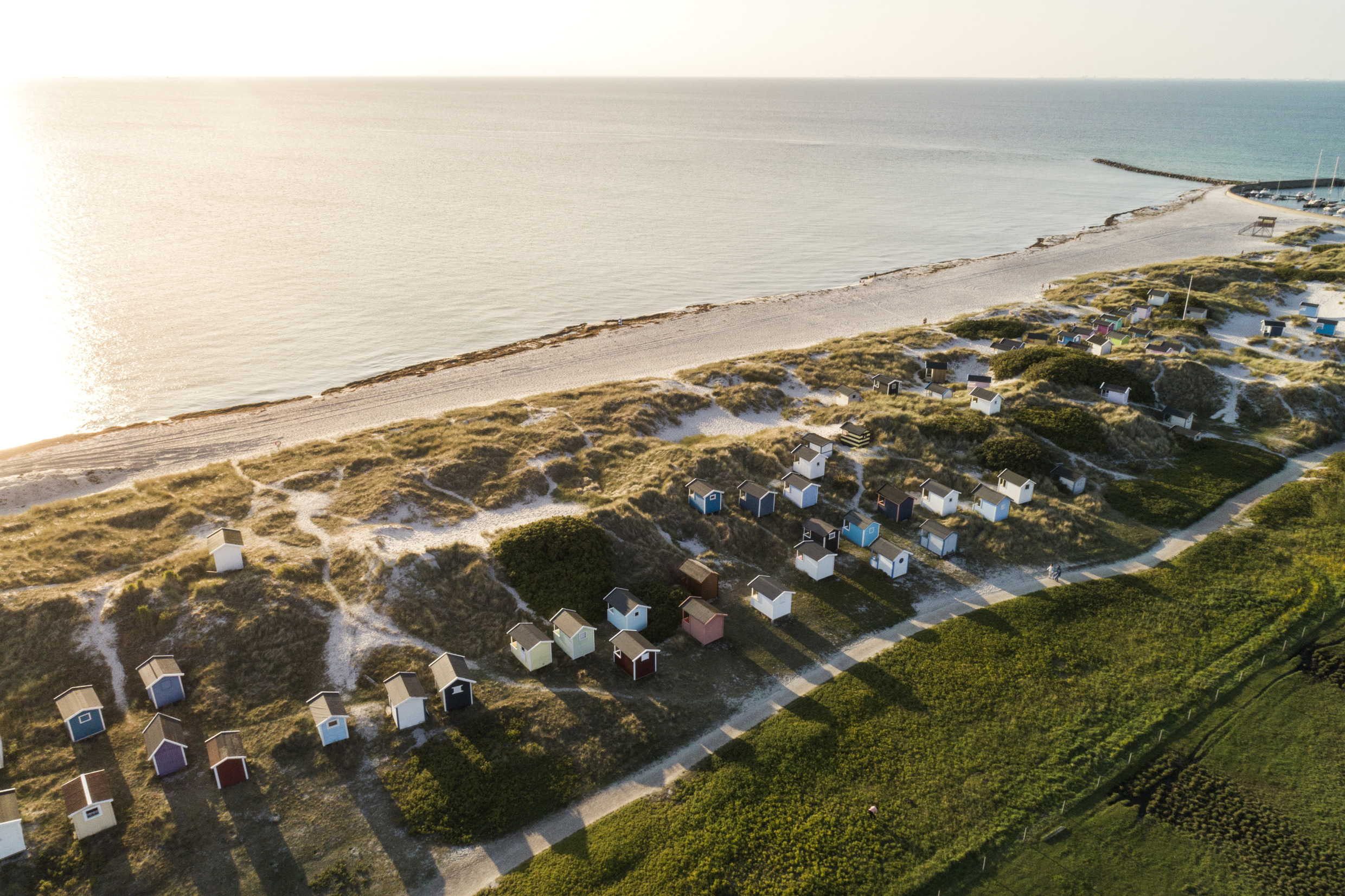 Vue aérienne d'une plage à côté de la mer avec de petits hangars à bateaux alignés le long du rivage.