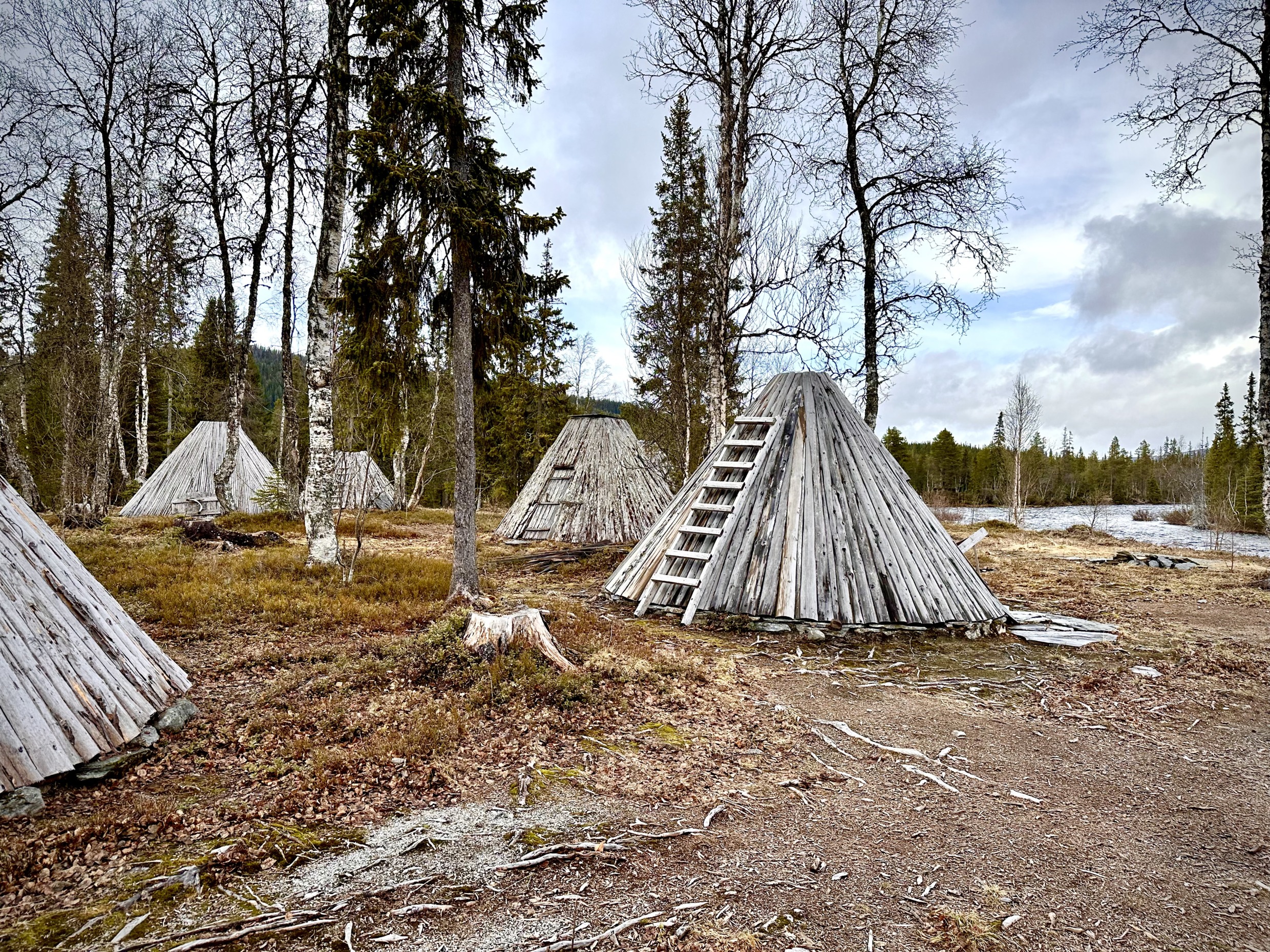 Five old wooden huts in the forest by a river.