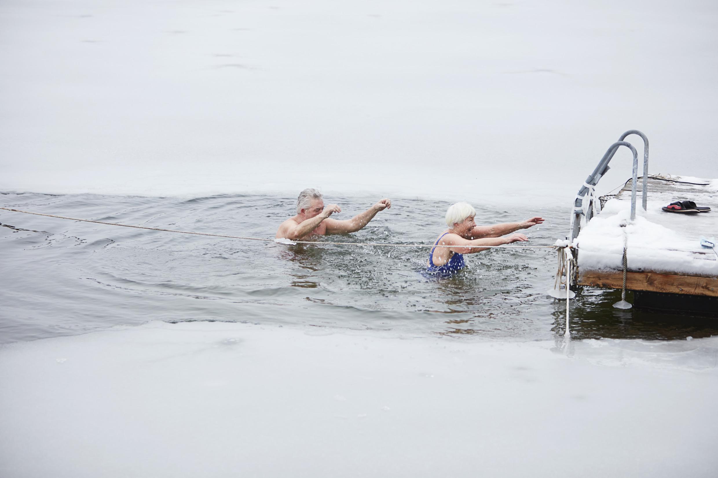 Un couple de personnes âgées se baignent dans un trou réalisé dans un lac recouvert de glace. Ils sont en train de retourner vers l'échelle sur la jetée.