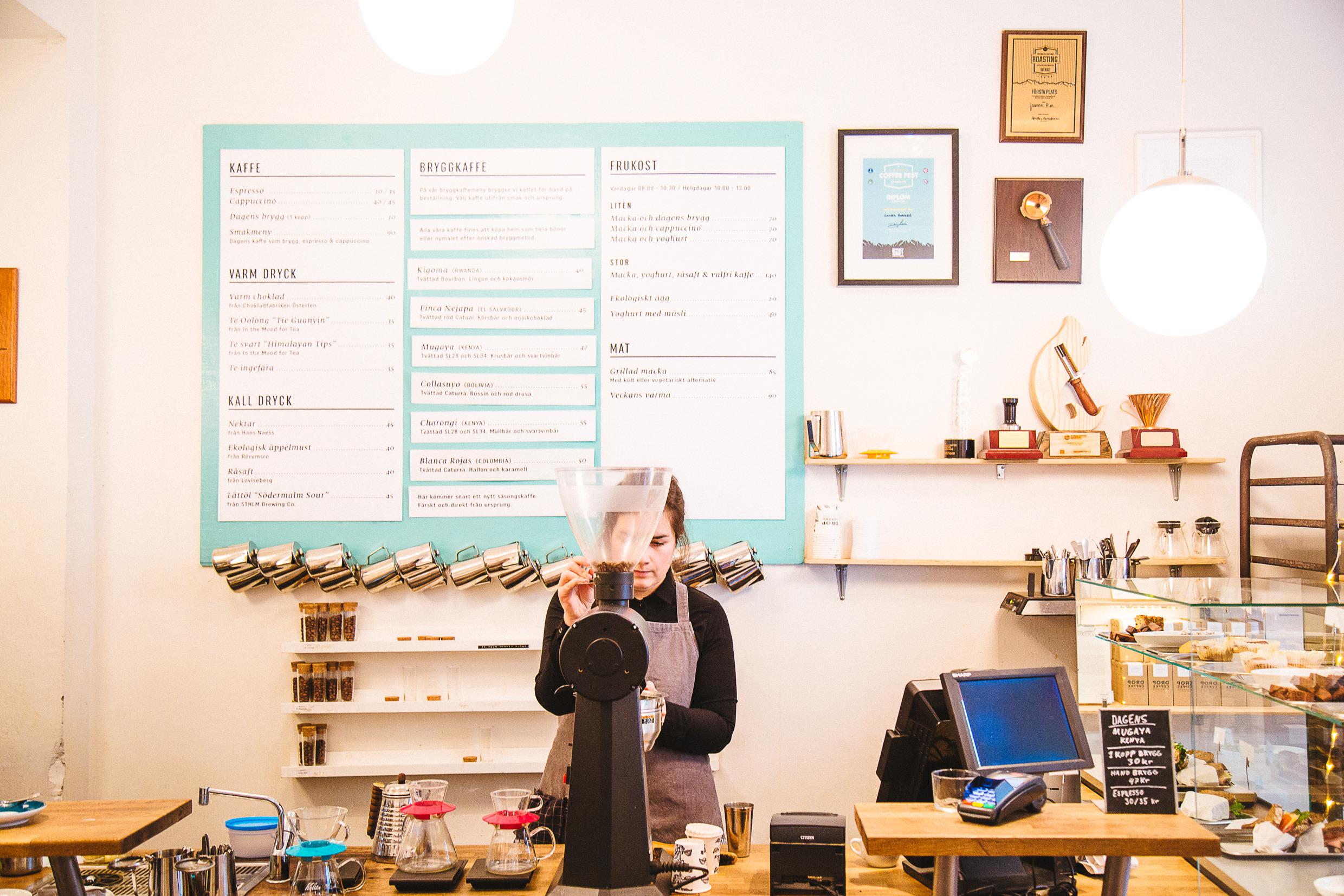 Een persoon staat achter de toonbank en is bezig met het malen van koffiebonen.