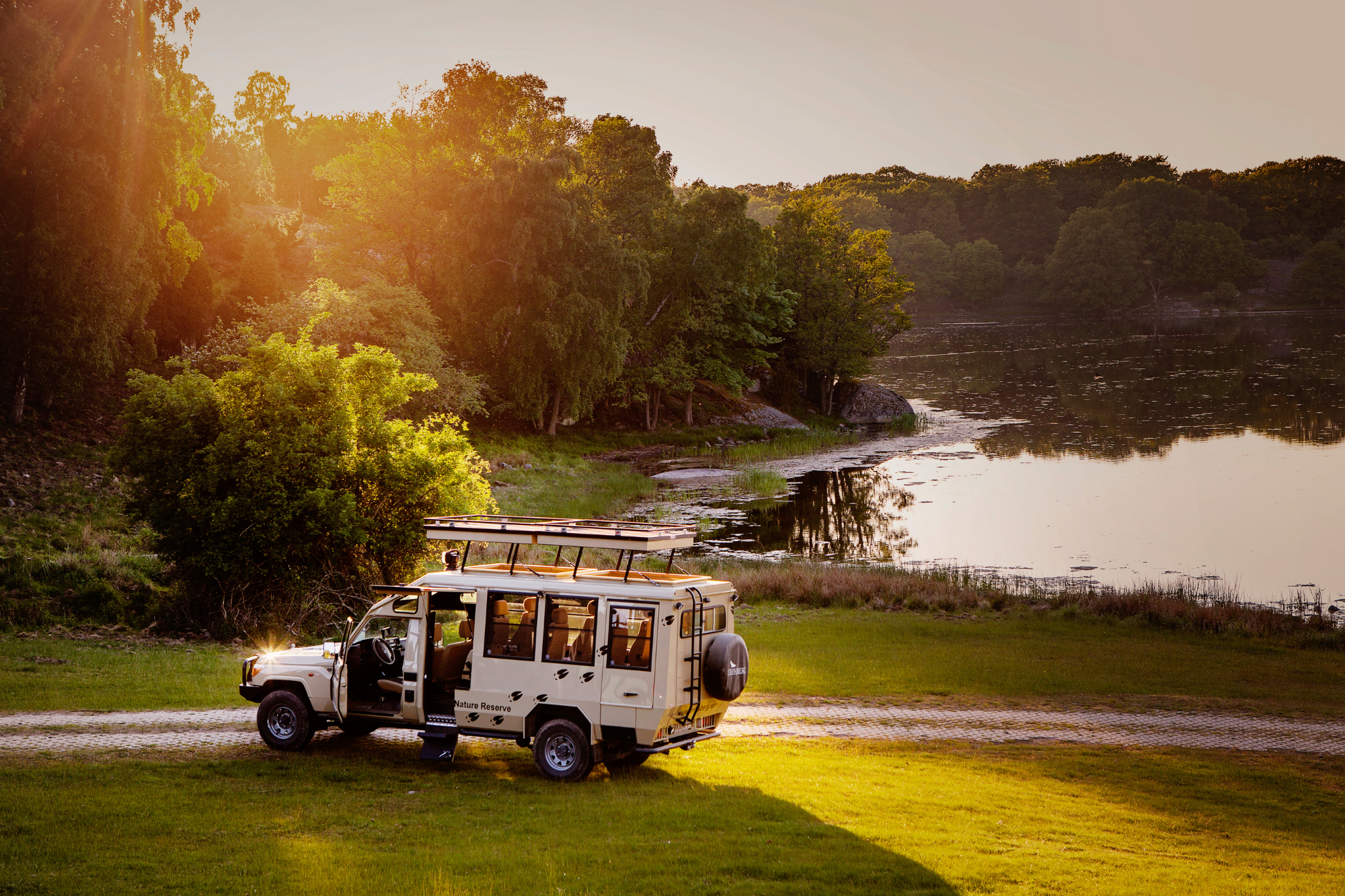 Een speciaal gebouwde safaribus bij Eriksberg Hotel & Nature Reserve, geparkeerd aan het water en in de zomer omringd door weelderige bomen.