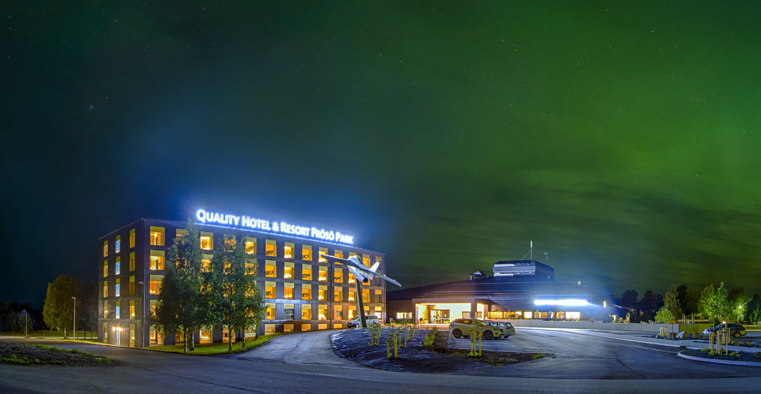 Das Frösö Park Hotel leuchtet nachts, während die Nordlichter am Himmel über ihm funkeln, und liegt in einer ruhigen Gegend in der Nähe von Östersund.