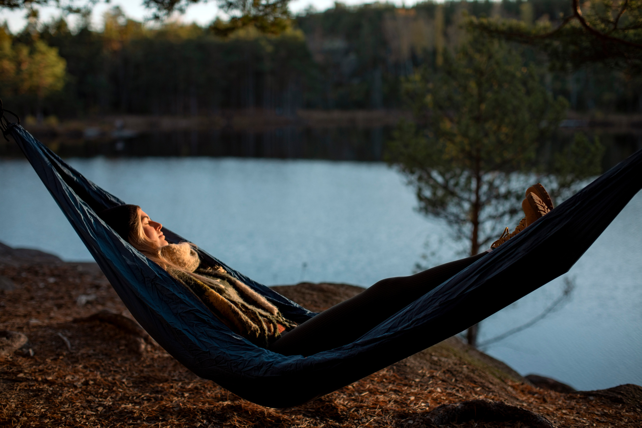 A woman is lying in a hammock by a lake.