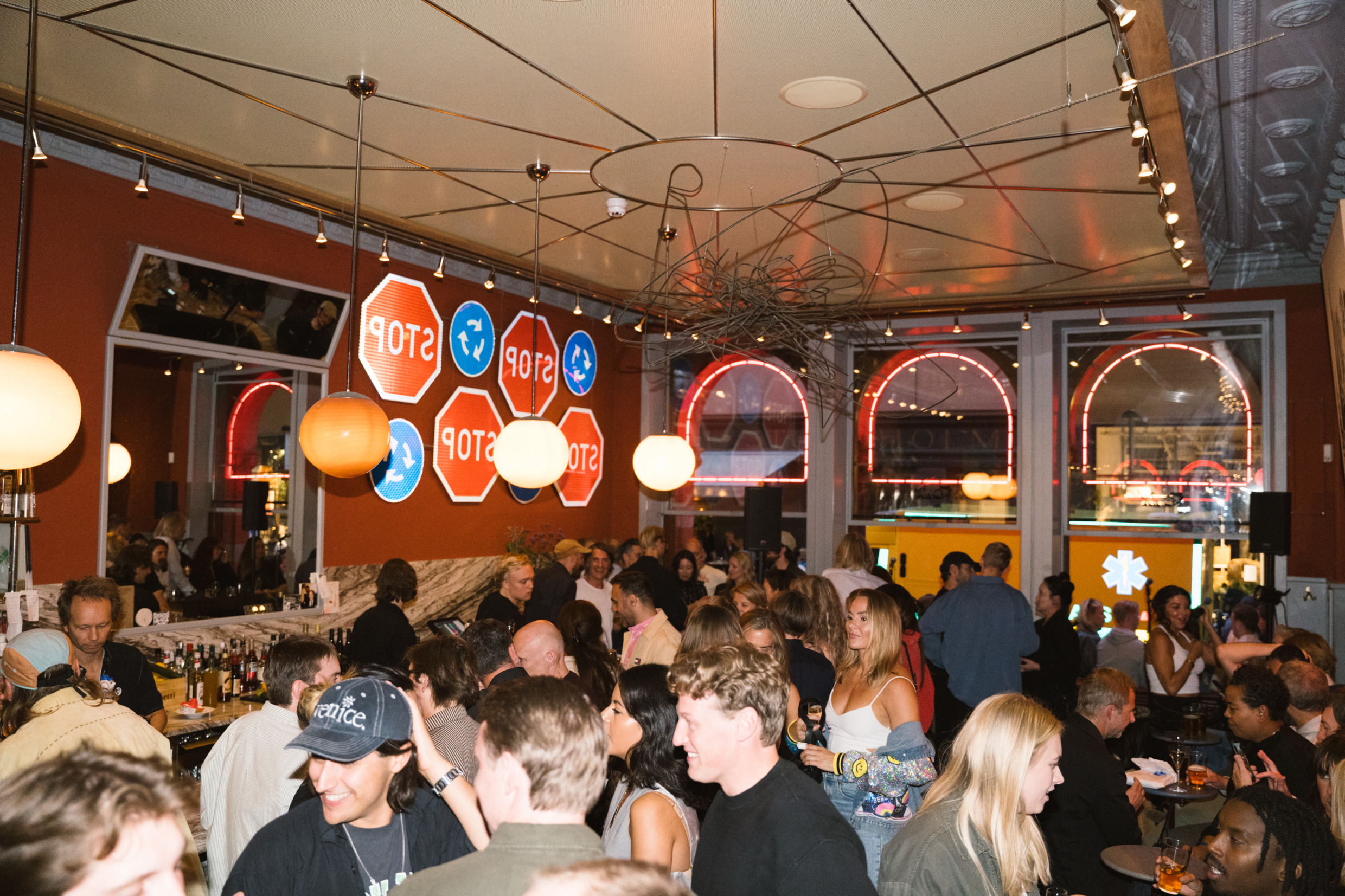 Drukte die geniet van een levendige avond bij Riche Fenix in Södermalm, Stockholm, met een drukke bar, moderne inrichting en oplichtende neonreclames op de achtergrond.