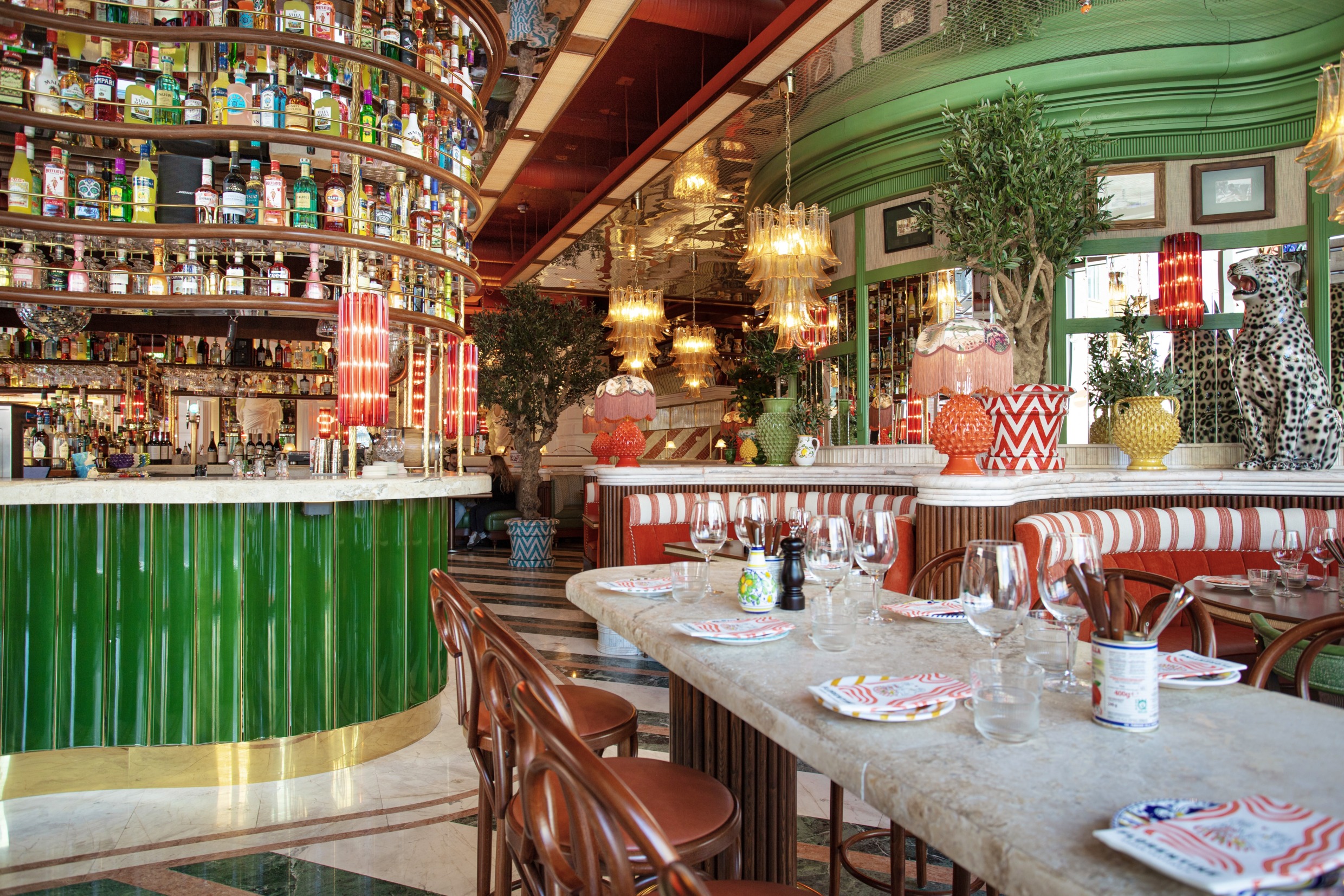 Vibrant interior of Florentine restaurant in Stockholm, featuring colourful decor, patterned cushions, glass lamps and a marble bar lined with bottles.