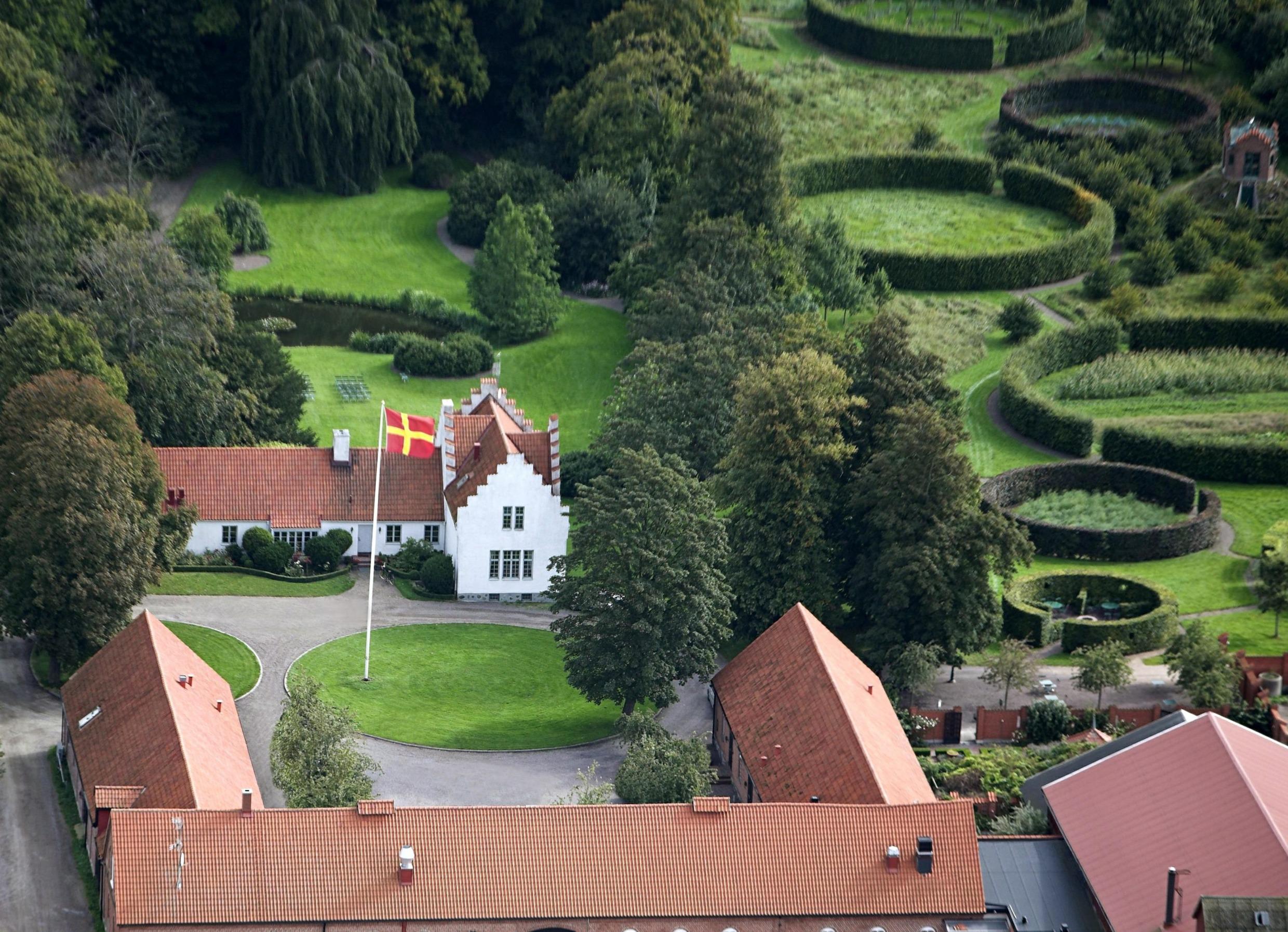 A aerial view over the farm Ängavallen. You see a white building,  the roof of the farmhouse and a beautiful green garden.