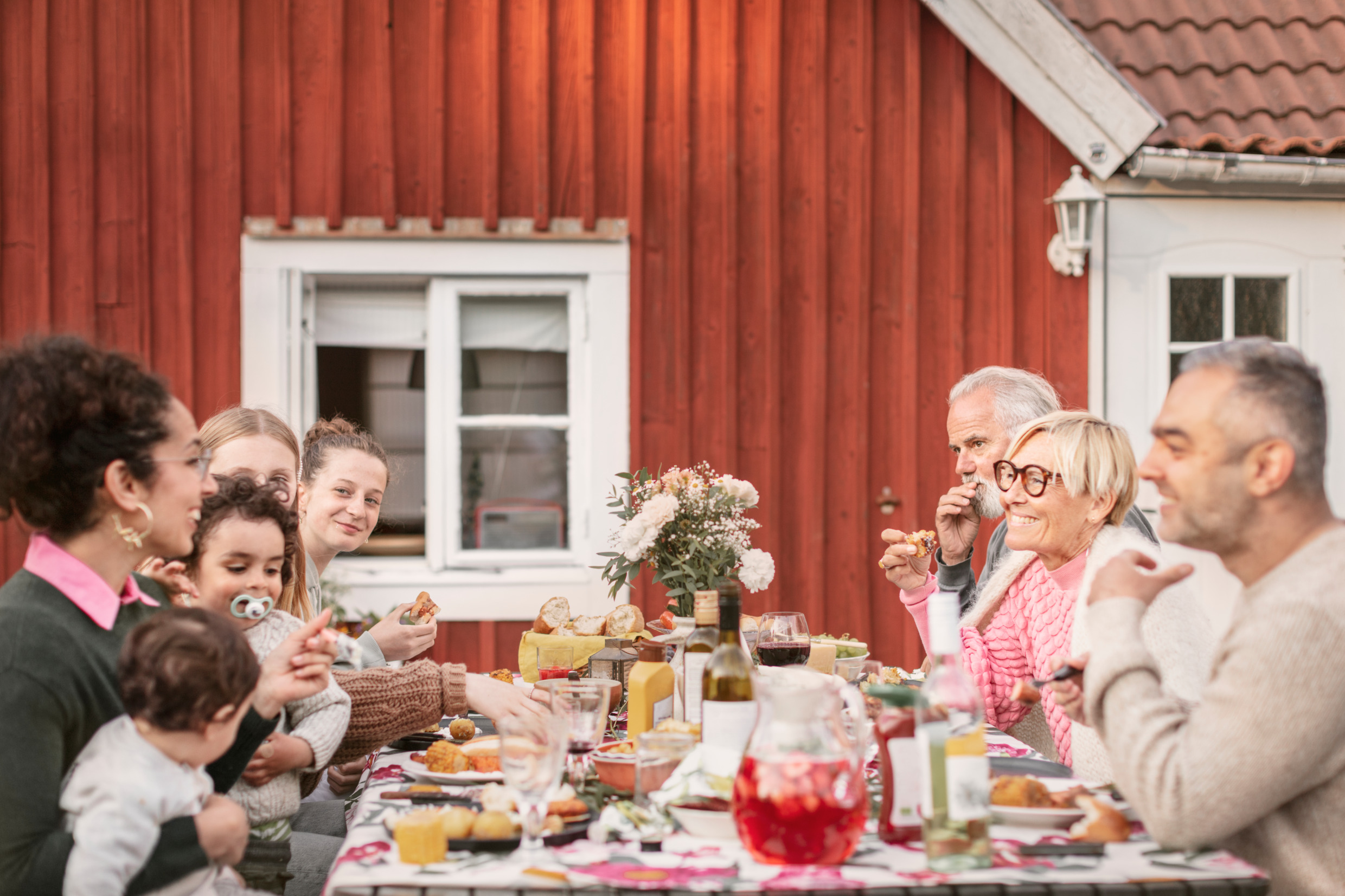 Menschen sitzen an einem Tisch im Freien vor einem Haus und essen und trinken.