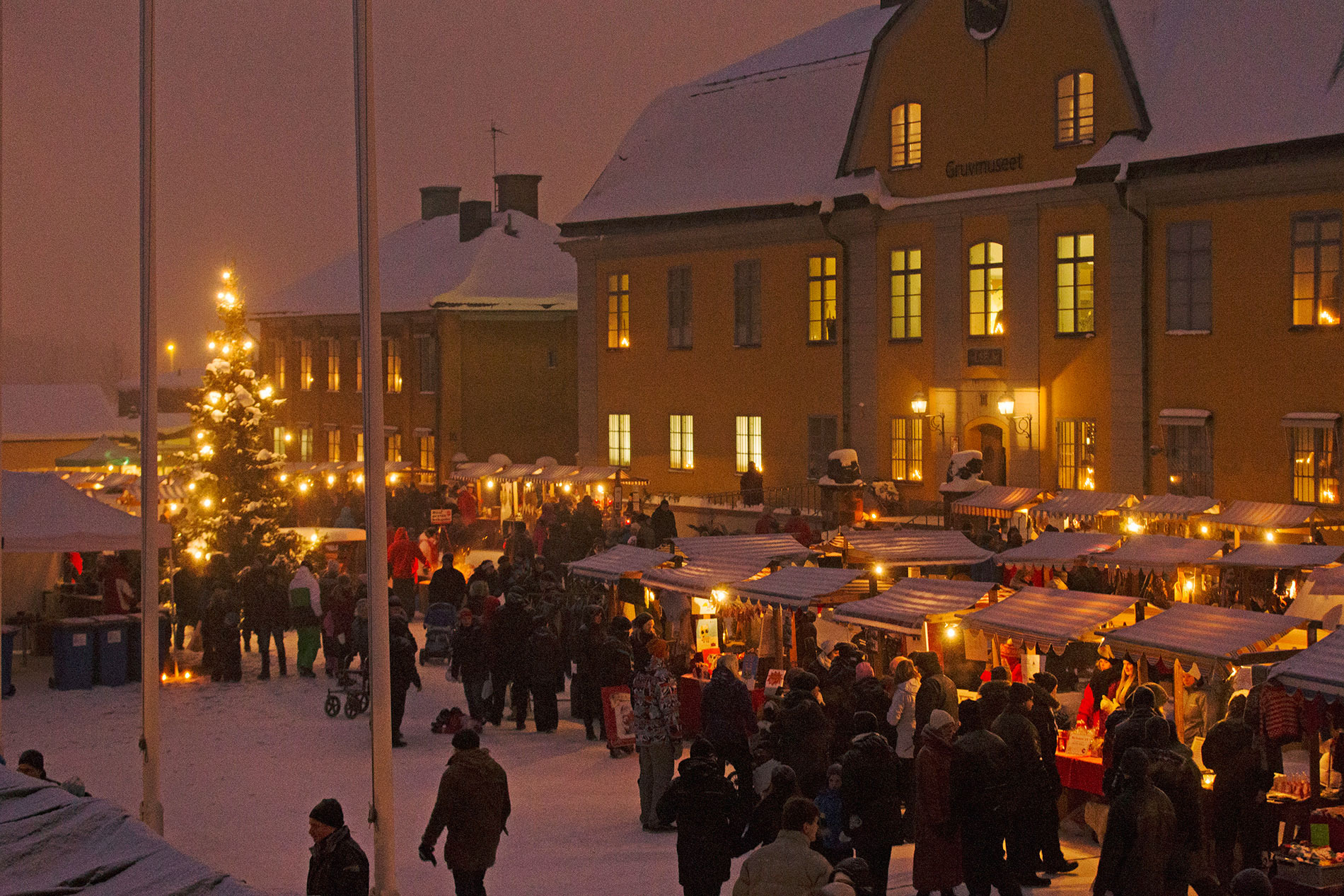 Une foule en train de flâner sur le marché de Noël de Falun au crépuscule, entourée de lumières, de stands et du musée de la mine.