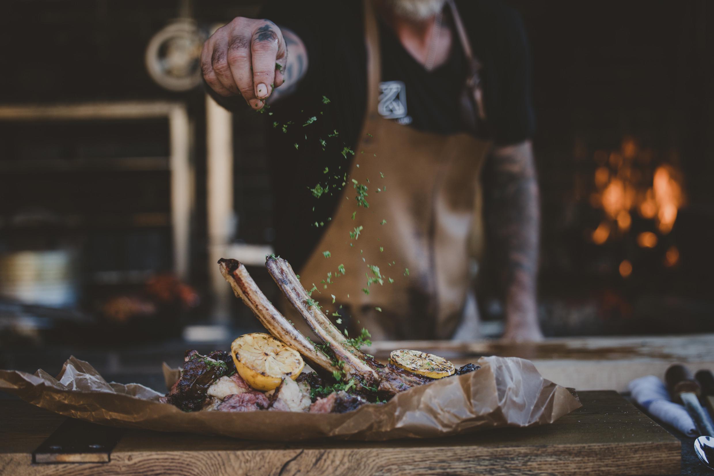 Ein Chefkoch würzt gegrilltes Fleisch.