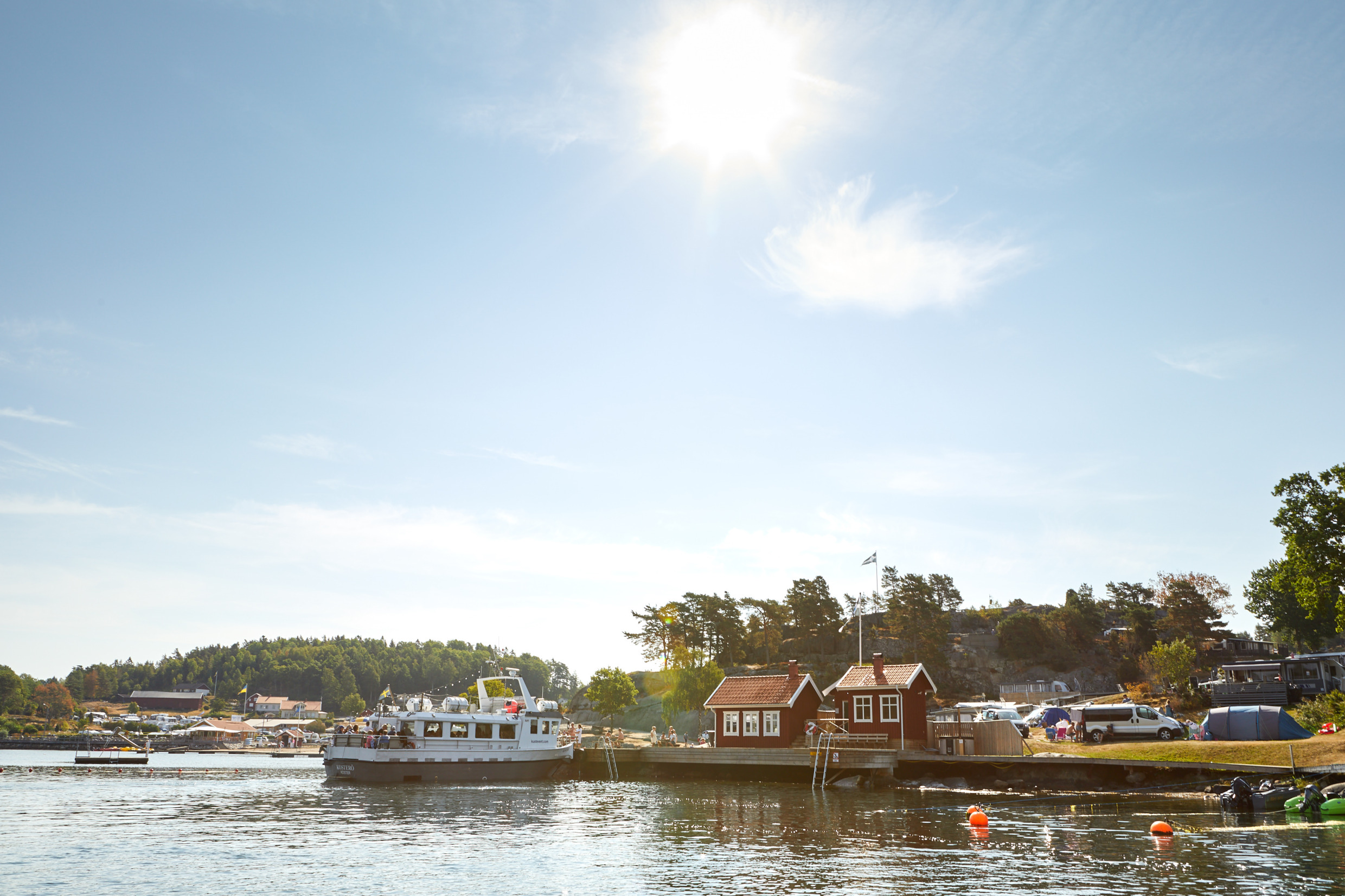 Een boot naast een steiger bij rode hutten tijdens een zonnige dag.