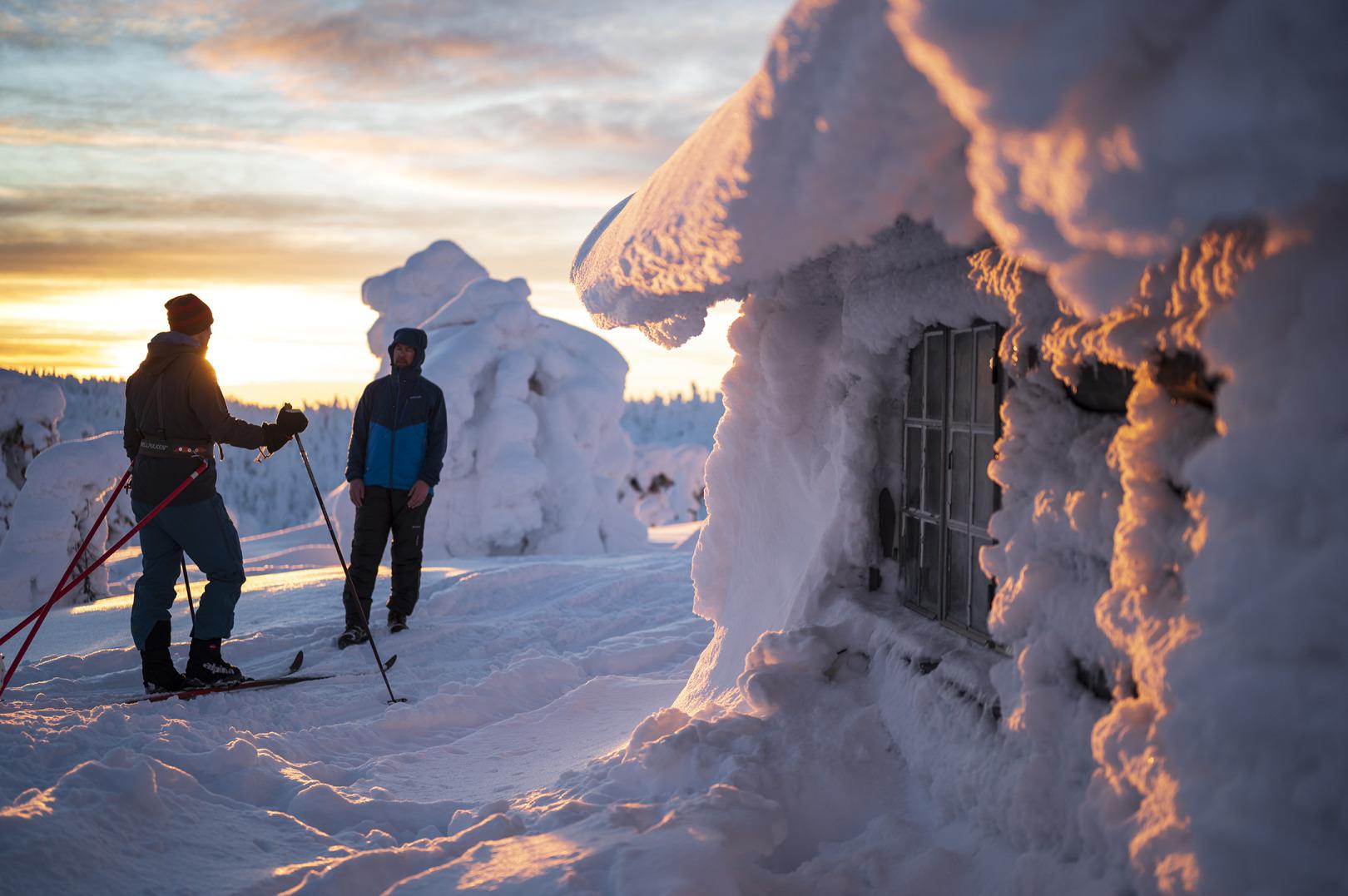 Toerskiërs bij een huisje in winterlandschap.