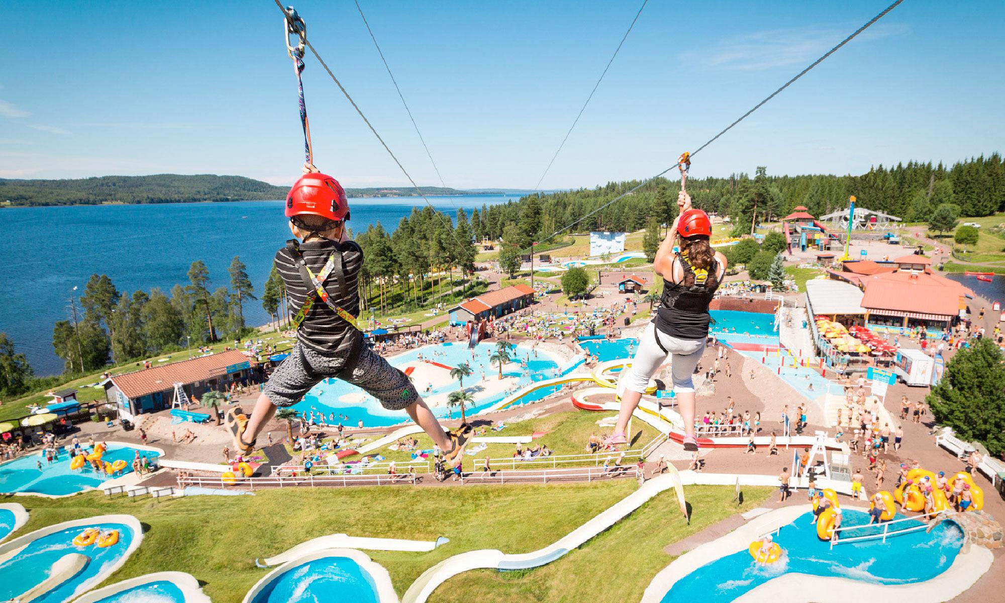 Zwei Kinder schwingen an einer Zippline über einen großen Wasserfreizeitpark.