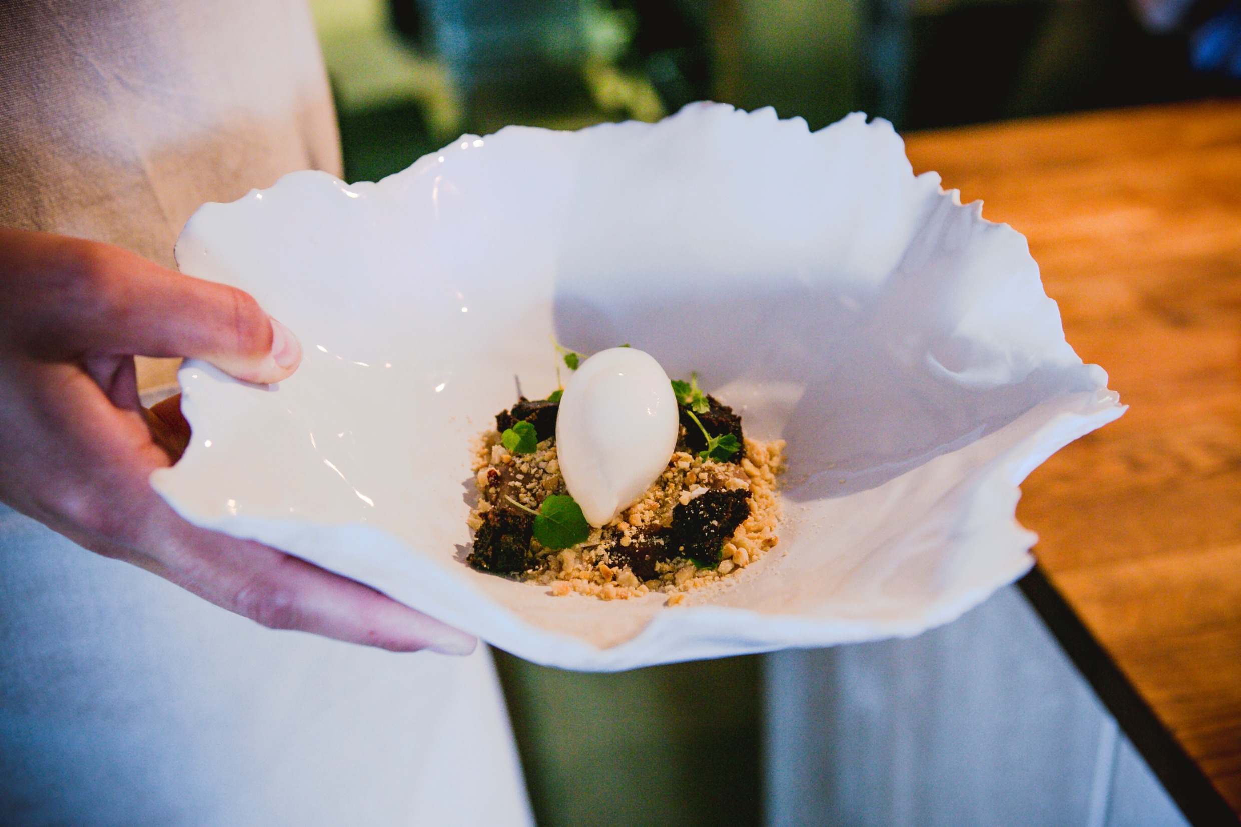 A hand holding a porcelain bowl with ice cream, crumble and fruit.