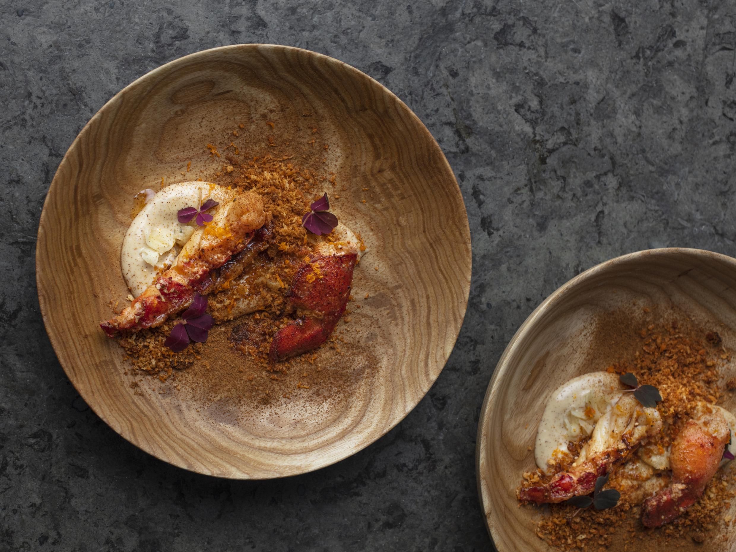 Zwei Holzteller mit sorgfältig anrichteten Speisen, verziert mit kleinen lila Blüten.