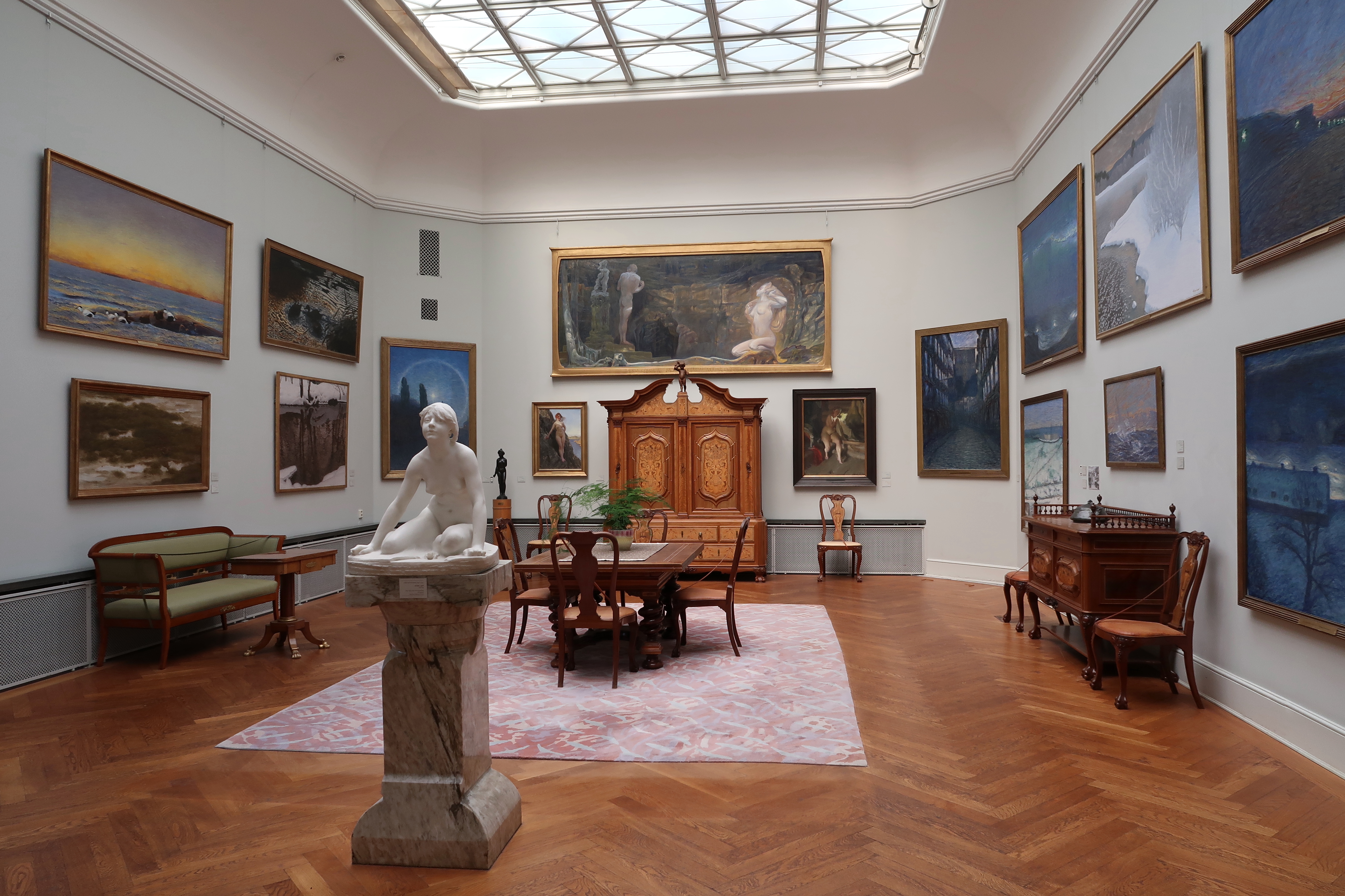 The dining room at the Thiel Gallery, with paintings covering the walls, a marble sculpture, antique wooden furniture and a large skylight.