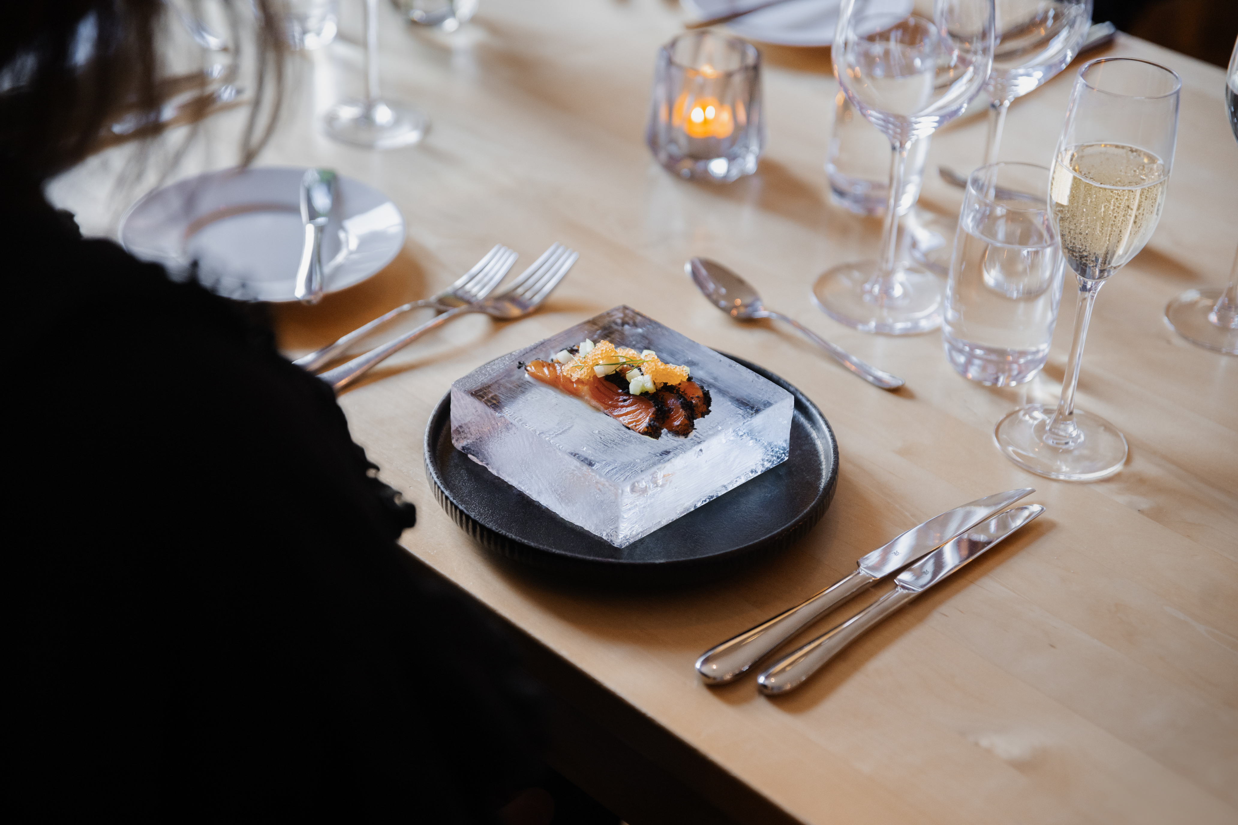 Ein schickes Gericht, das im Icehotel auf einem Eisblock serviert wird, zusammen mit Gläsern und Besteck auf einem Restauranttisch.