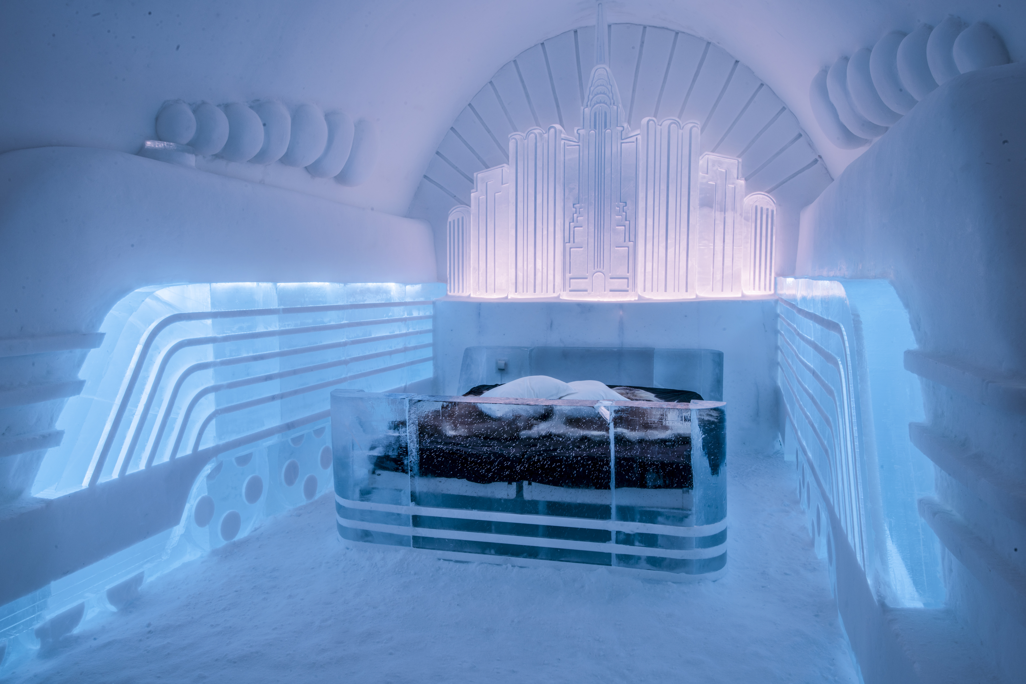 Een kunstsuite in het Icehotel met een ijsbed en verlichte ijssculpturen in een kamer die volledig uit sneeuw en ijs bestaat.