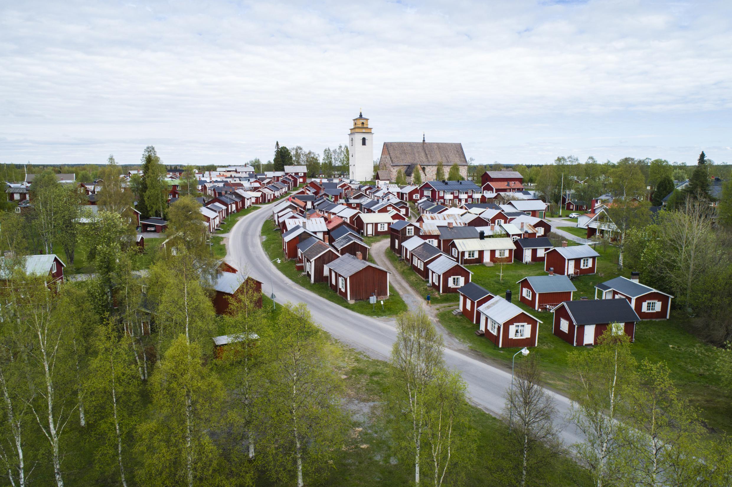 Des chalets rouges entourent une vieille église en pierre avec un clocher blanc.