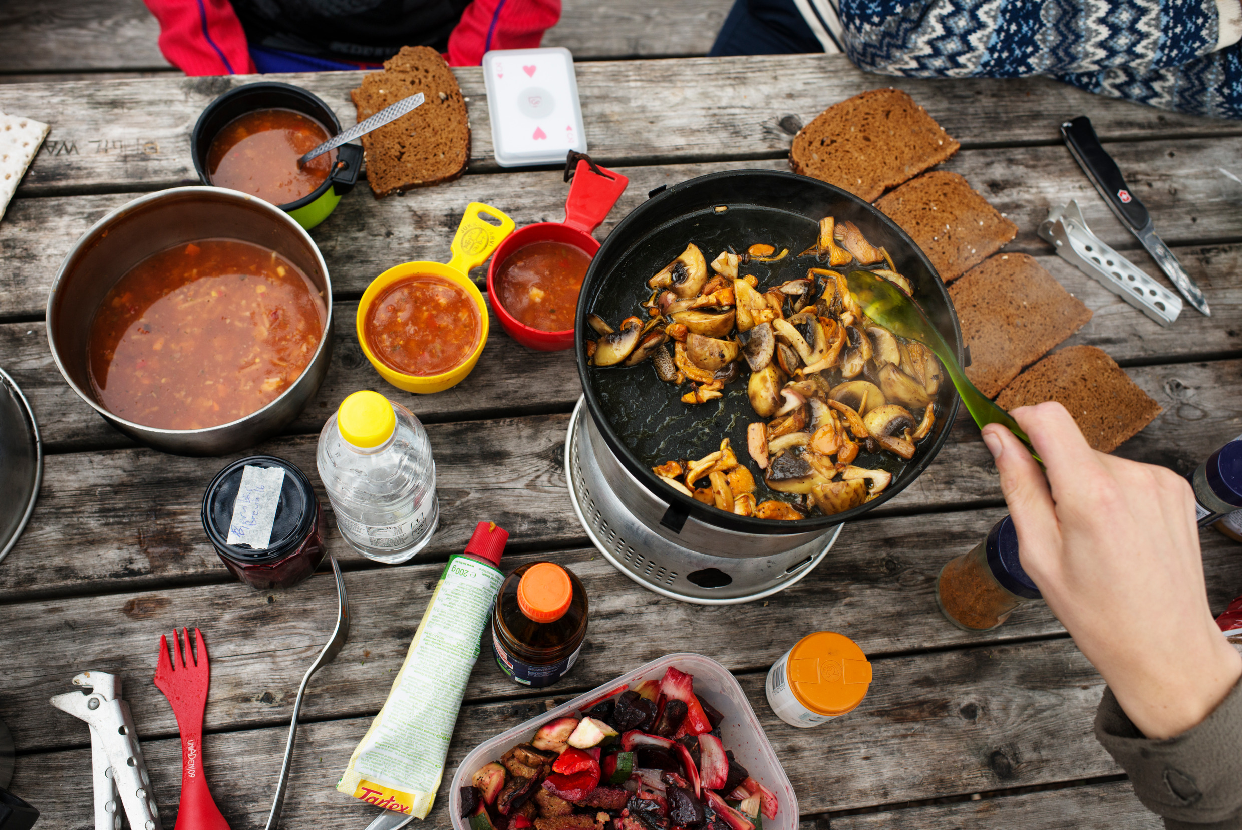 Ein Wanderessen mit Tomatensuppe, Brot und selbstgesammelten Pilzen auf einem Holztisch.