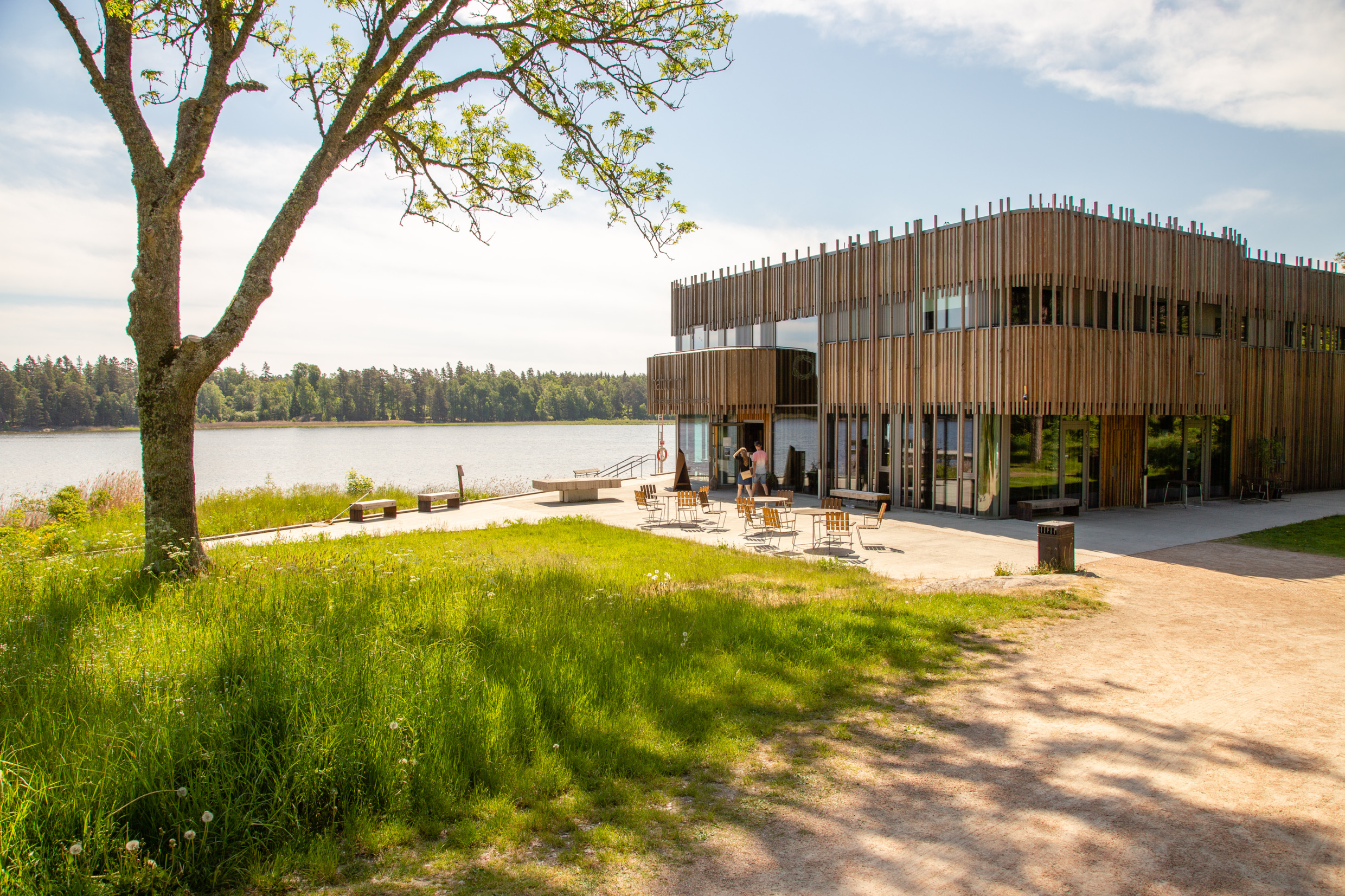 Naturum Vänerskärgården Victoriahuset bei strahlendem Sonnenschein mit zwei Personen, die draußen spazieren gehen.