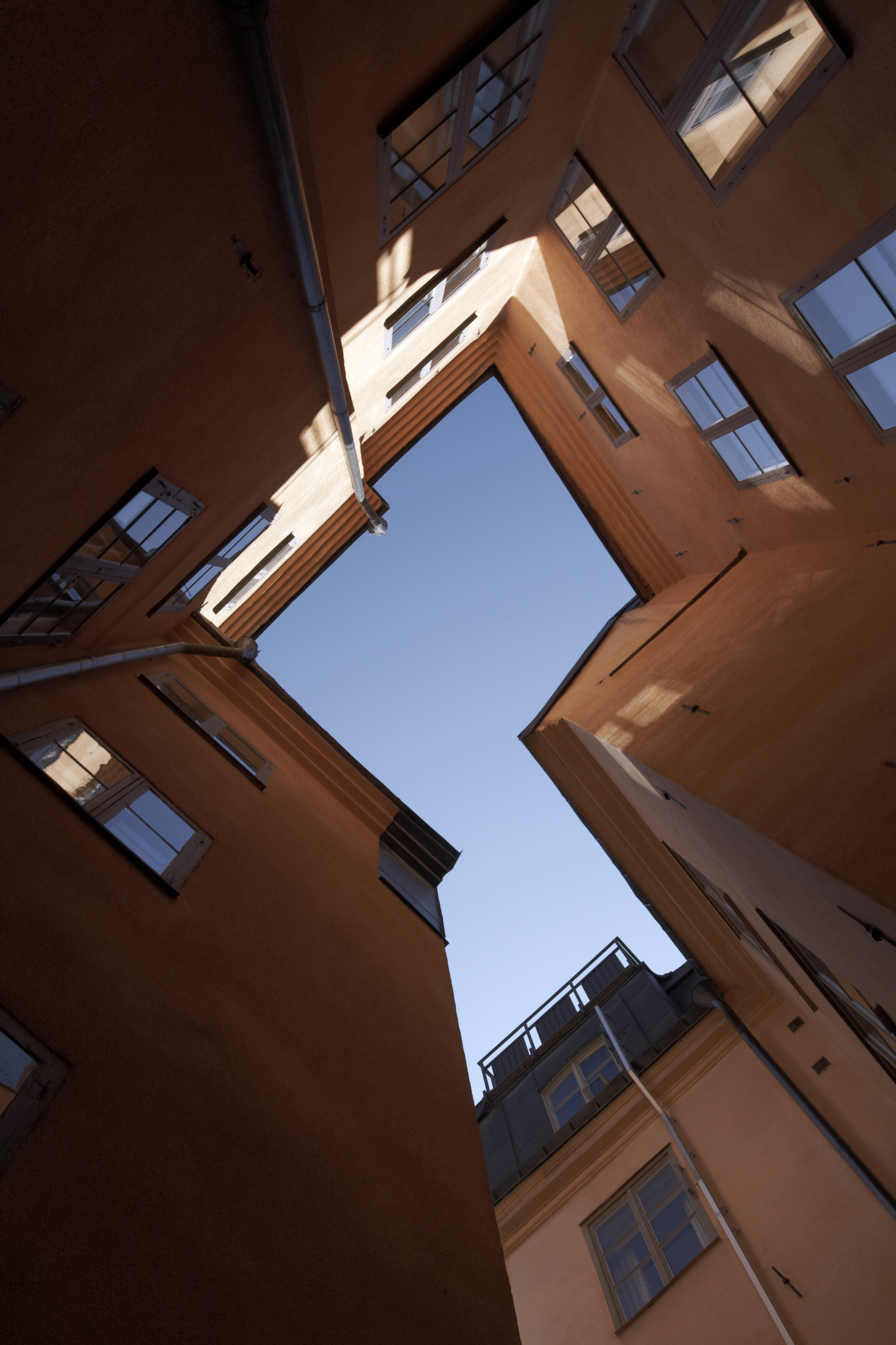 View looking up between warm orange buildings in a narrow Gamla Stan courtyard, framing a clear blue sky above.