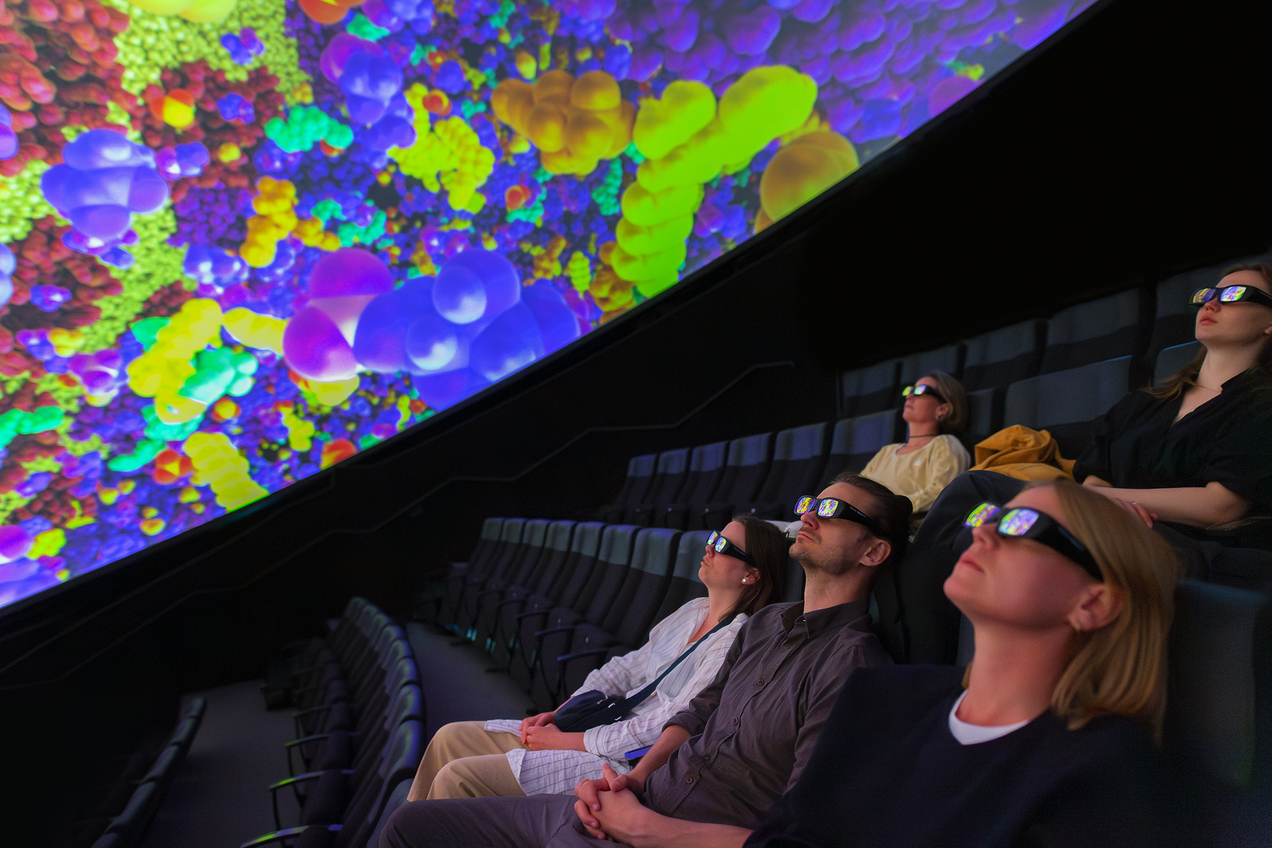 Eine Gruppe von Menschen mit 3D-Brillen sitzt auf Stühlen und schaut auf die Leinwand im Wisdome Stockholm.