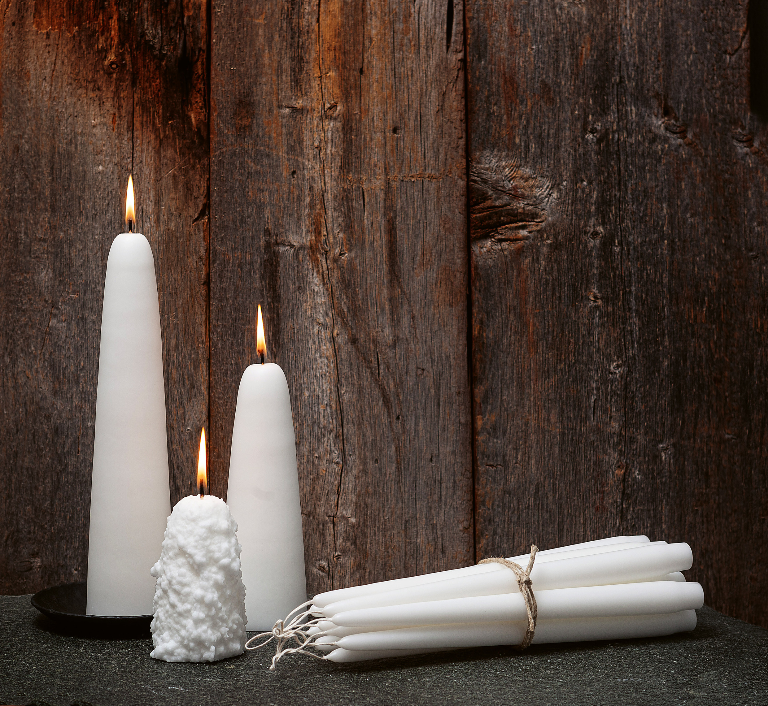 Weiße handgemachte Kerzen, darunter das charakteristische Schneeball-Design, sind vor einer rustikalen Holzwand bei Åre Ljusfabrik ausgestellt.