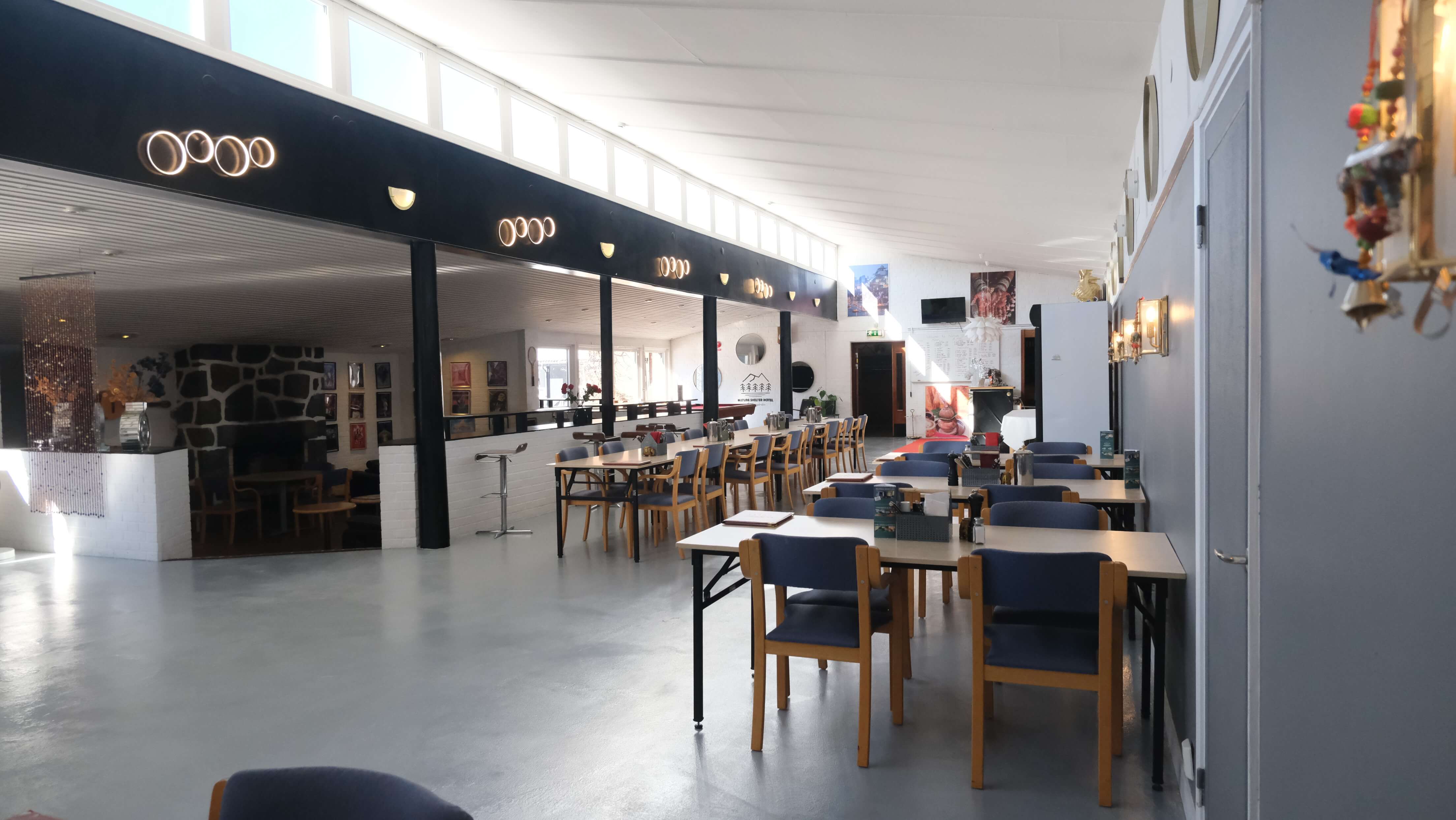 A dining area with tables, chairs and carpets on a dark-coloured floor.