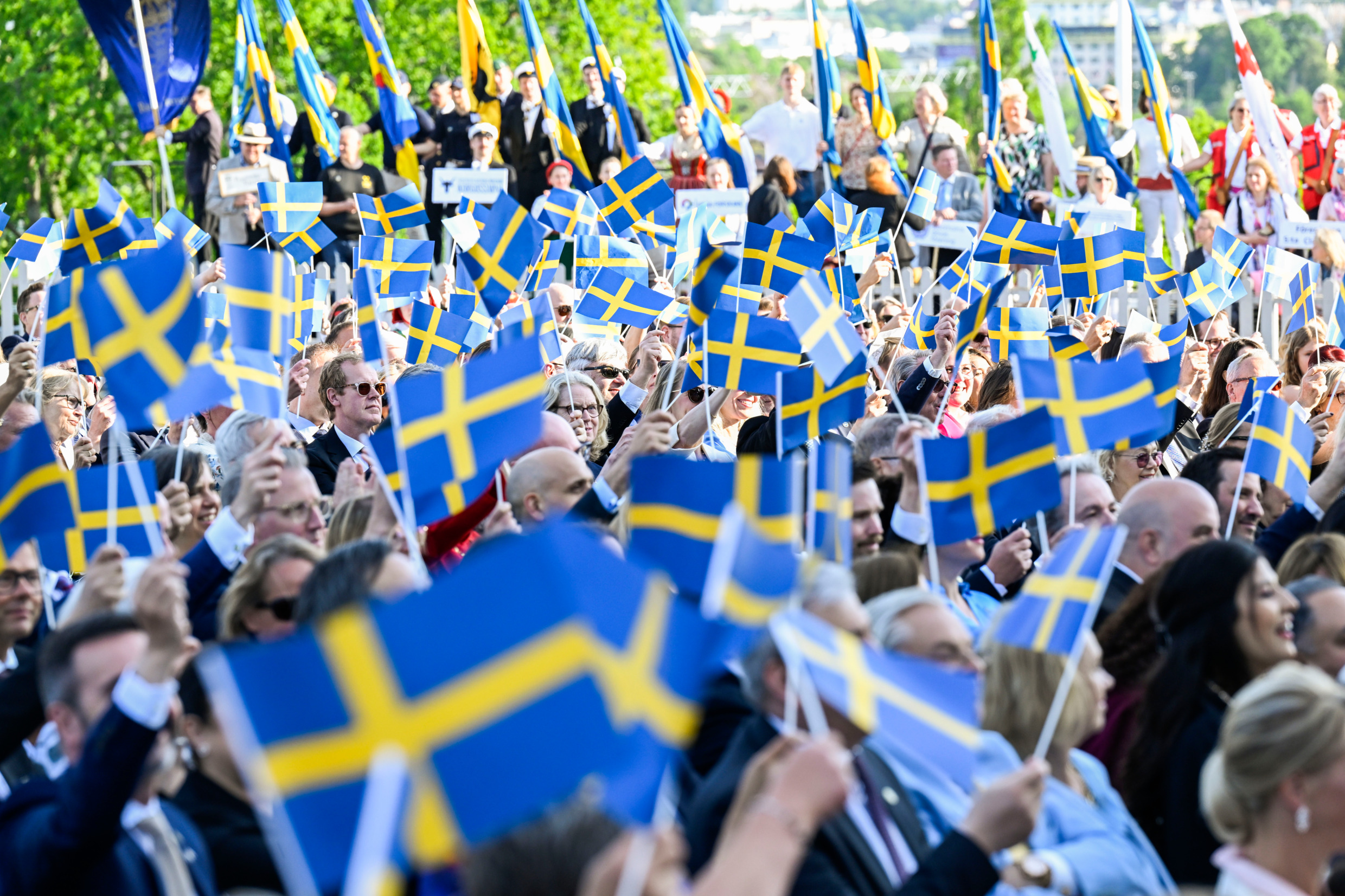 A crowd of people waving Sweden's blue and yellow flag.