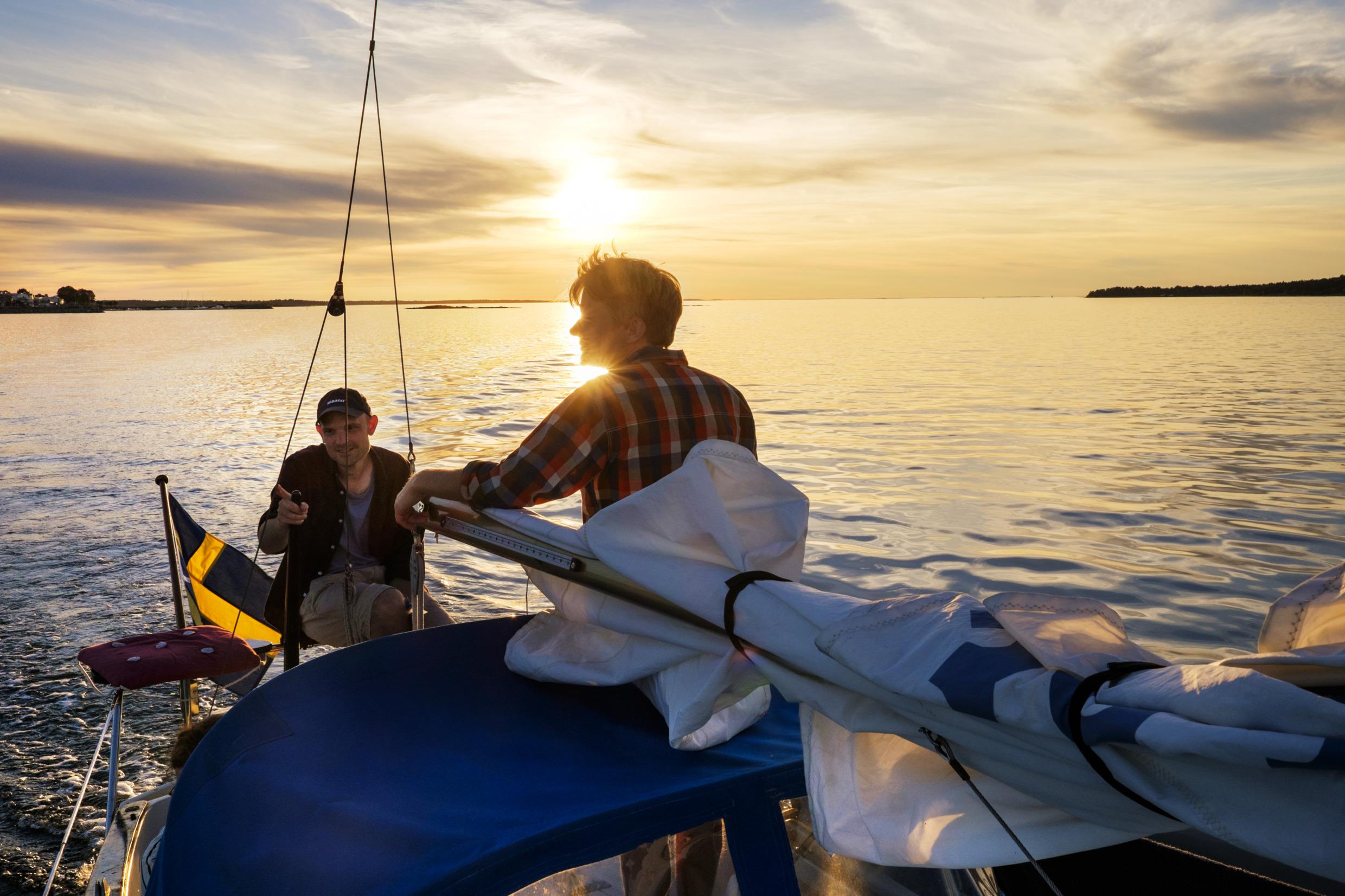Twee personen op een zeilboot bij de ondergaande zon.