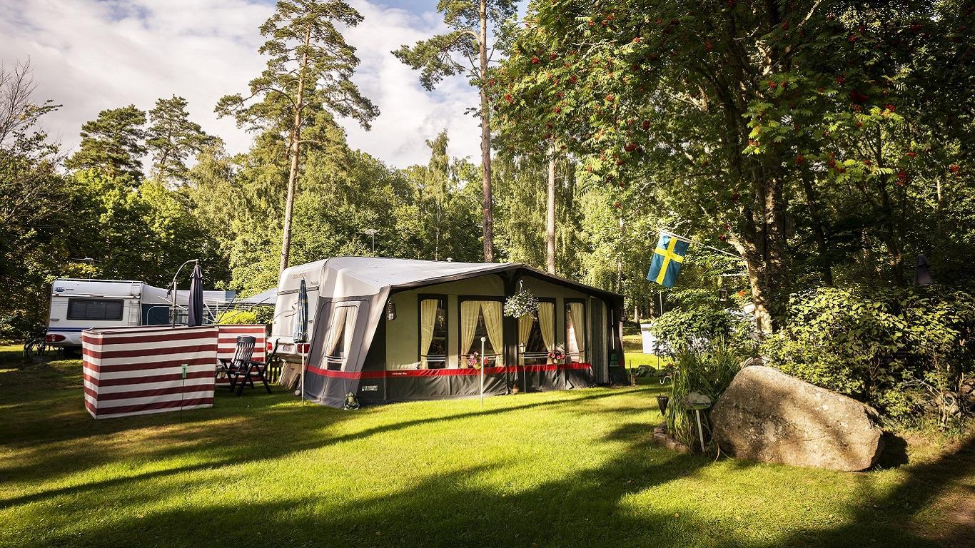 Een tent en een camper op een kampeerplaats bij First Camp Stensö, omringd door groene bomen en de rustige natuurlijke omgeving van de camping.